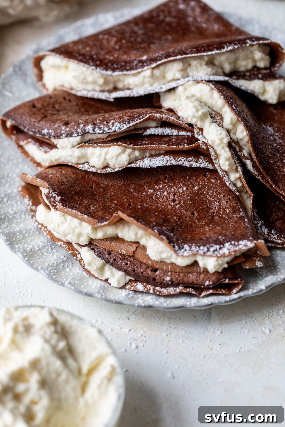 folded chocolate crepes stuffed with whipped cream on a plate, garnished with powdered sugar