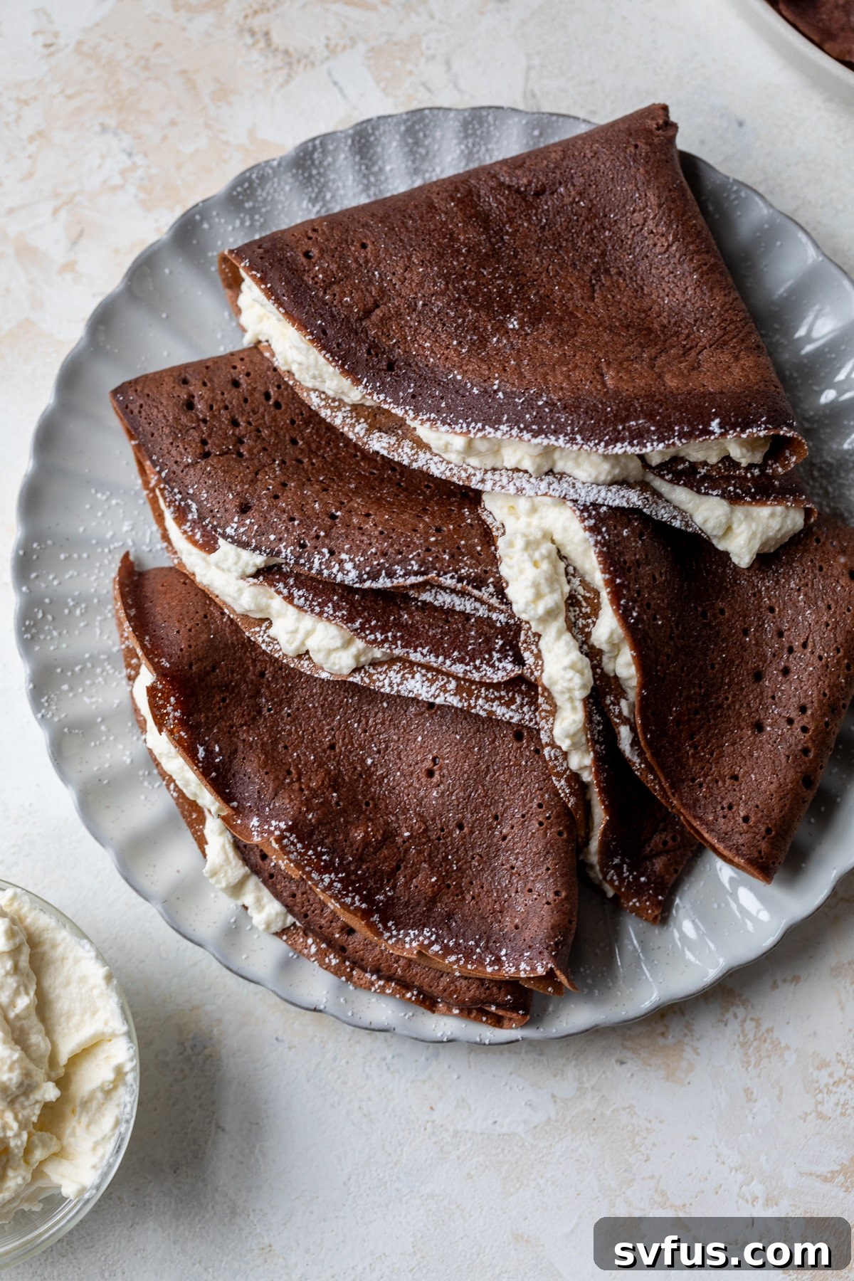 an overhead view of multiple chocolate crepes stuffed with whipped cream on a white plate