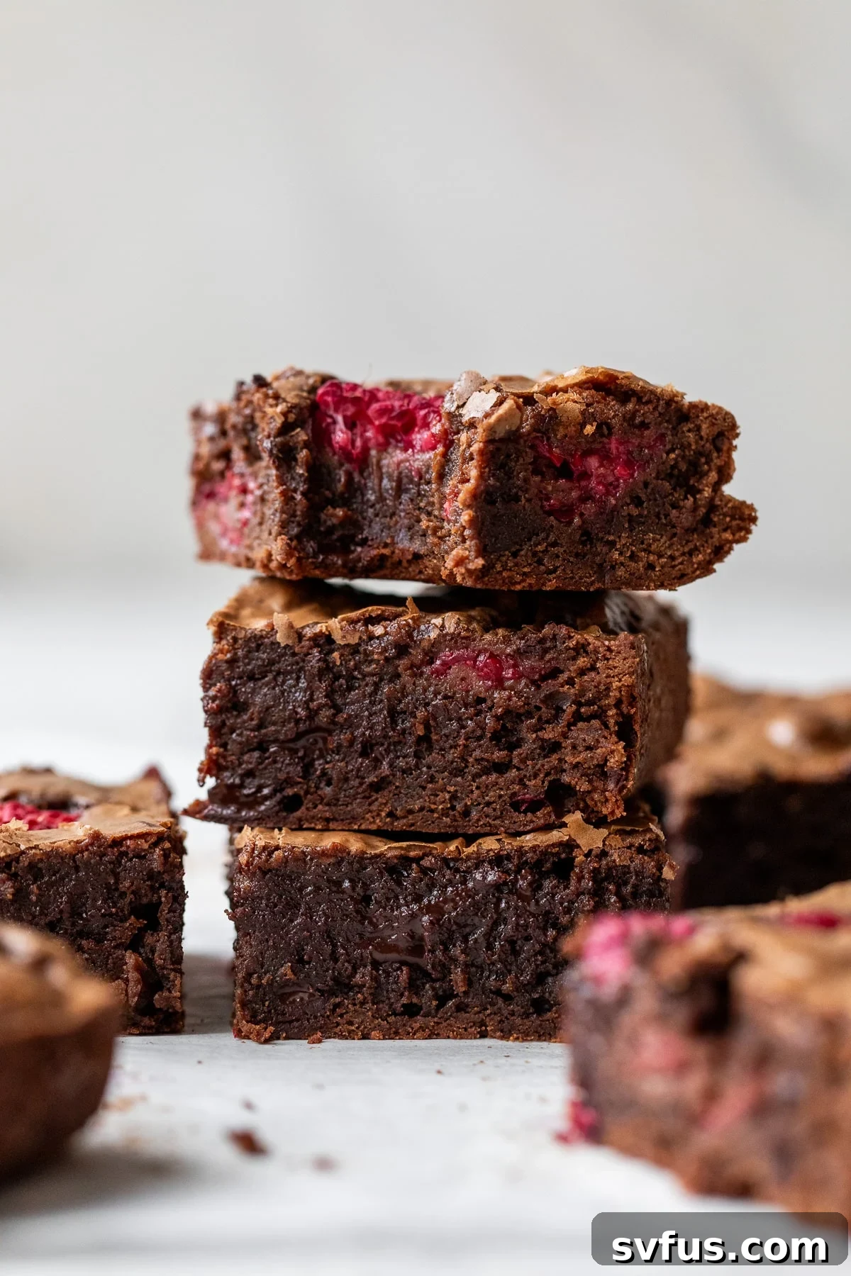 Three decadent chocolate raspberry brownies stacked, showing their fudgy texture and fresh raspberries.