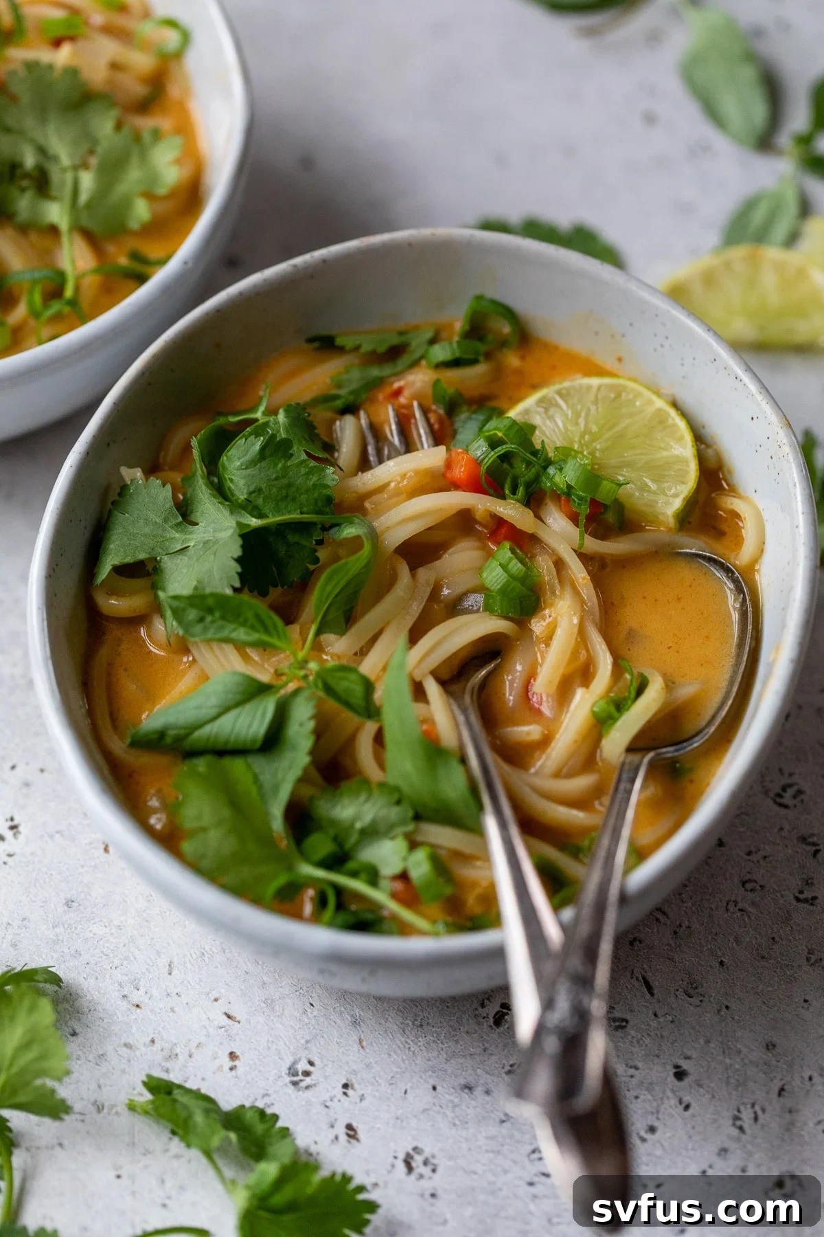A steaming bowl of vegan red curry noodle soup, garnished with fresh herbs and a fork ready to scoop
