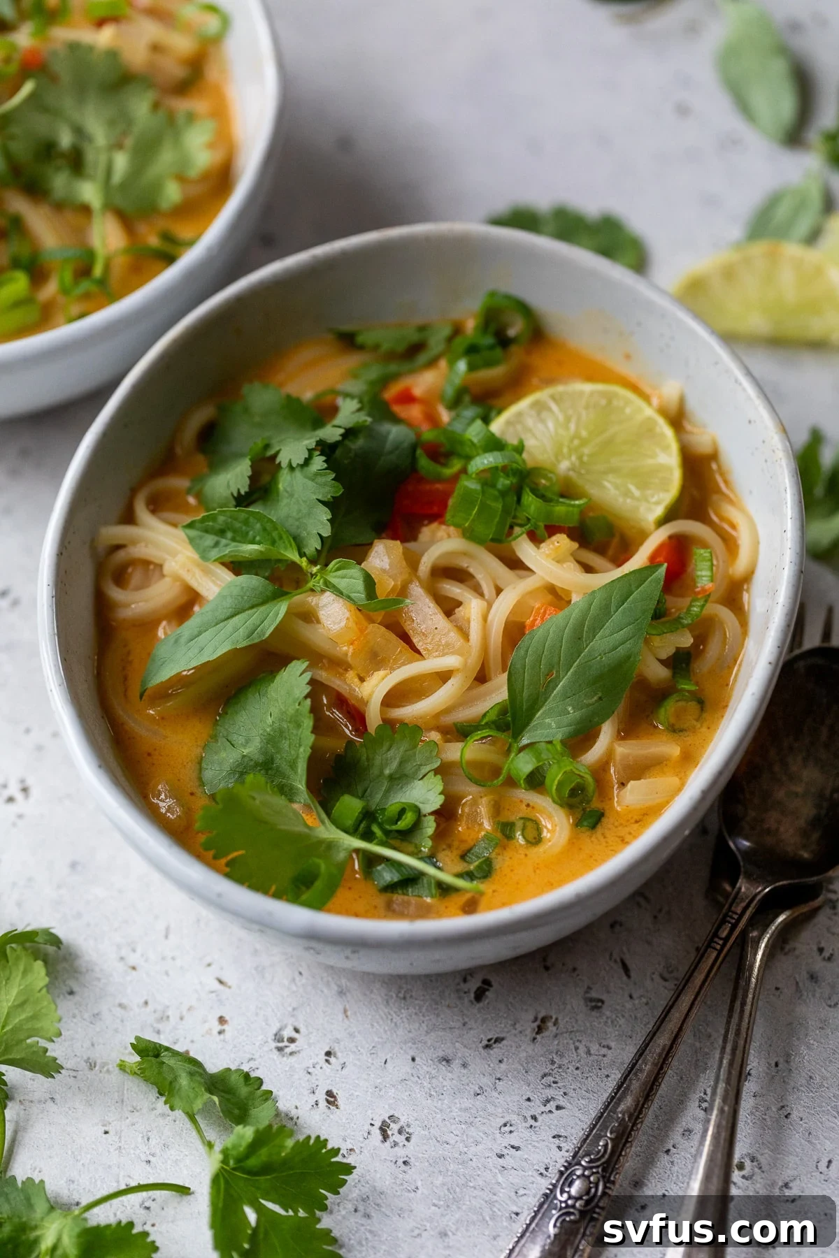 curry noodle soup in a bowl with a fork and spoon beside it