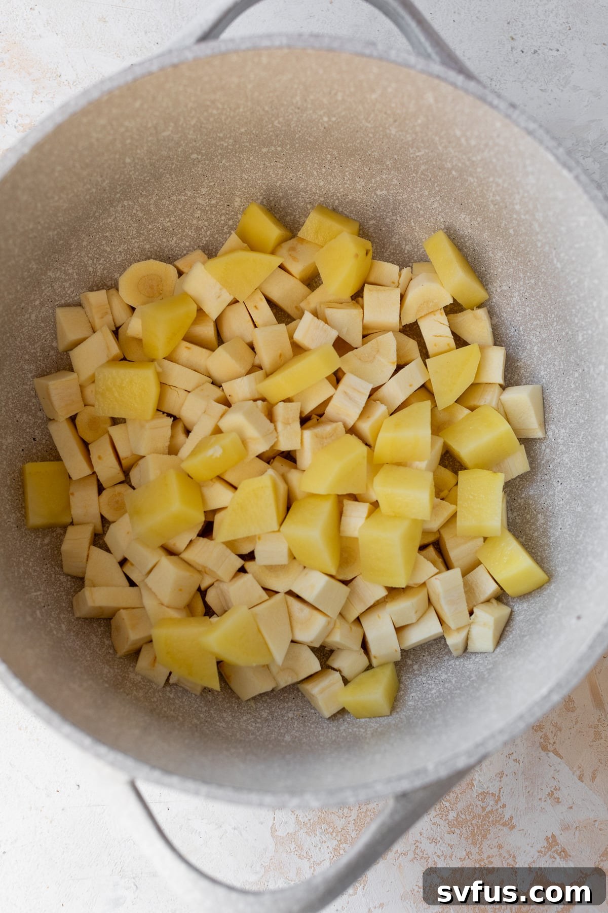 Cubed parsnips and potatoes simmering in a pot of water on the stove.