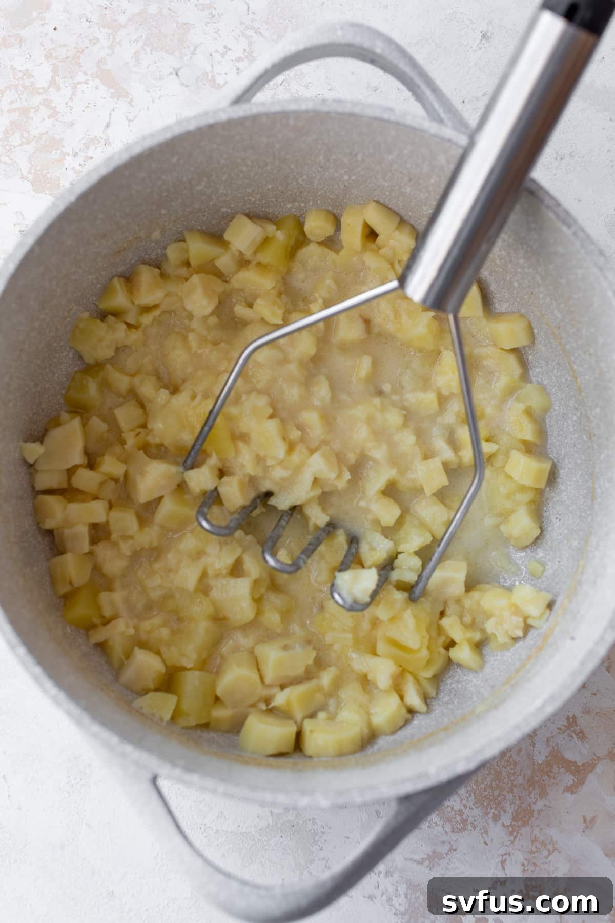 Mashed parsnips and potatoes being mashed in a bowl with garlic, milk, and butter.