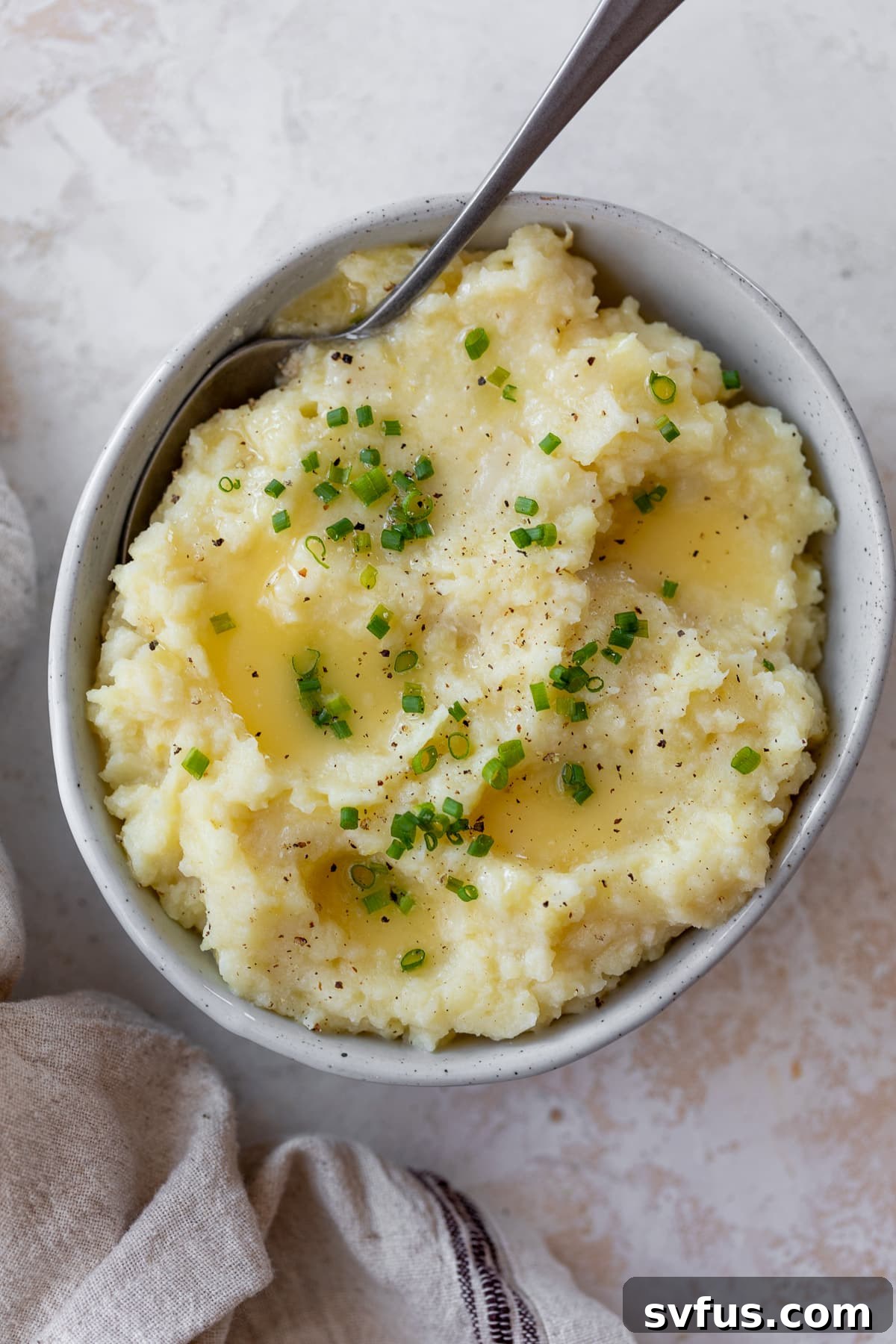 A beautifully presented bowl of mashed parsnips with a spoon, garnished with fresh herbs.