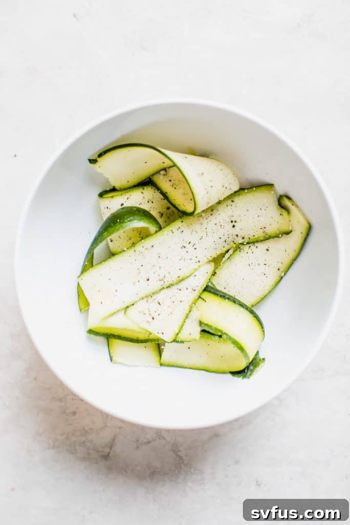 Fresh zucchini ribbons arranged on a white pizza base with ricotta and tomatoes
