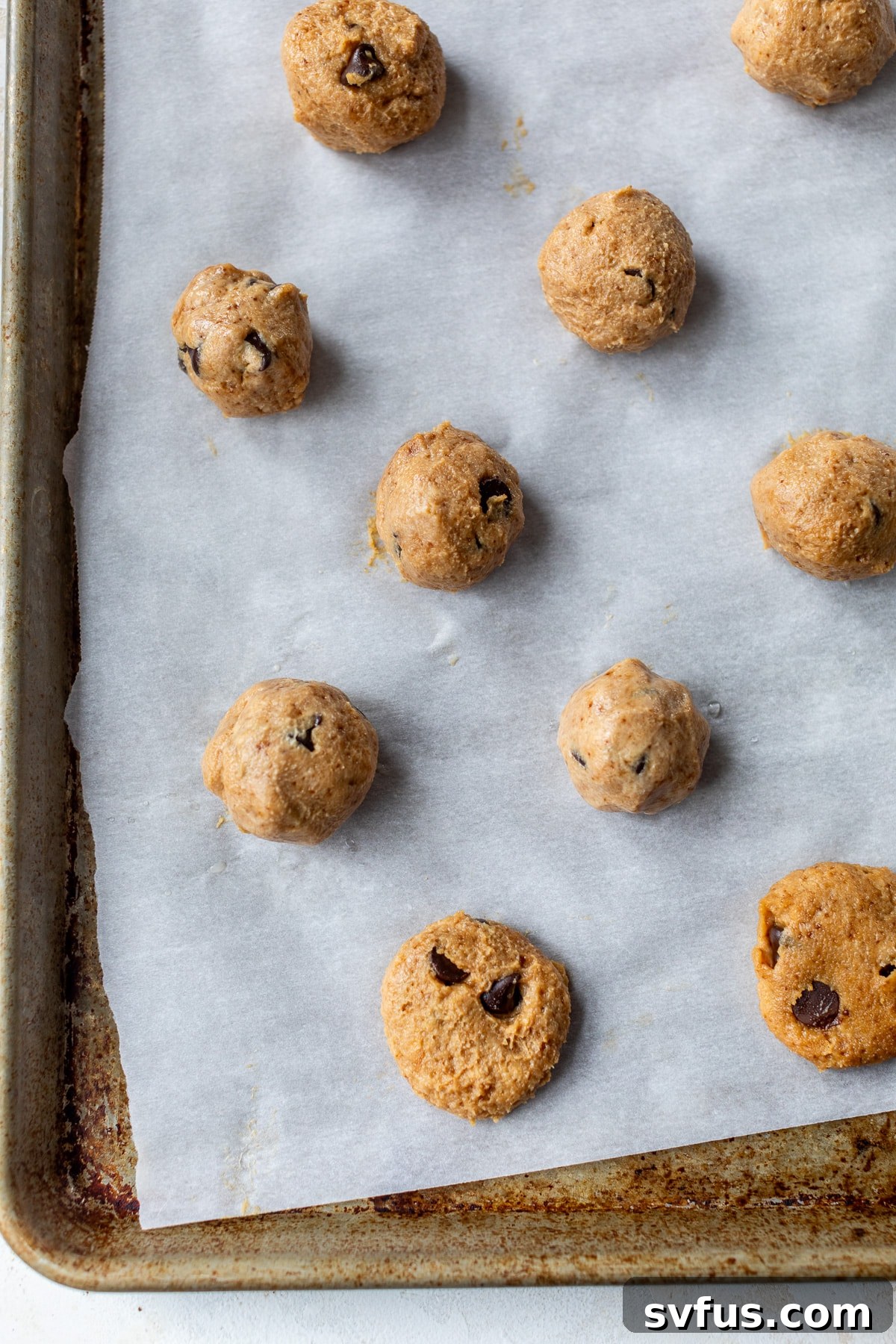 cookie dough balls flattened on a parchment-lined baking sheet, ready to bake