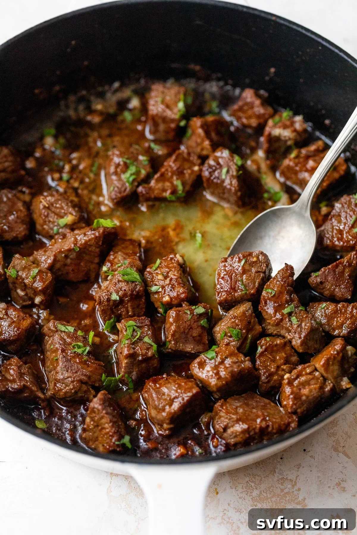 Sizzling Cajun Steak Bites in a cast iron skillet, ready to be served, with a spoon nestled in the savory sauce.