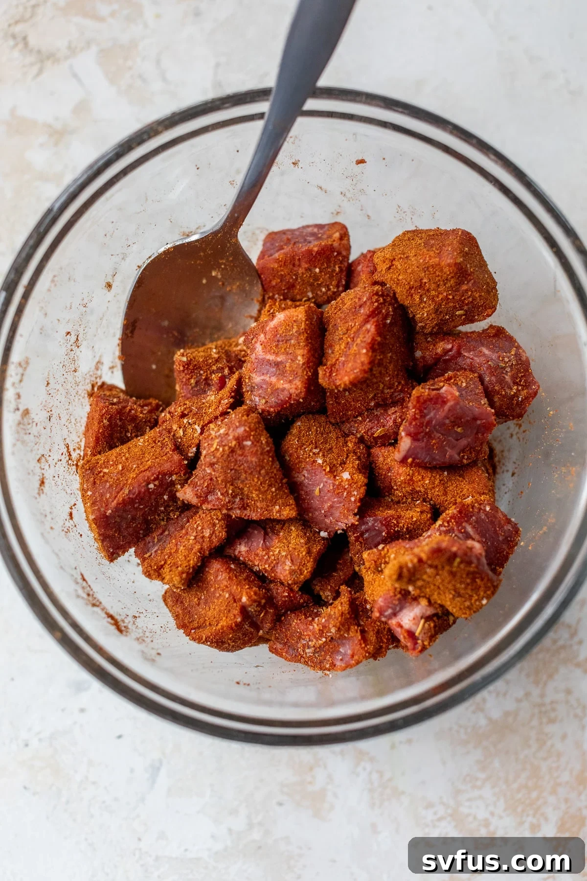 Raw steak pieces in a bowl, coated with a vibrant Cajun seasoning rub, ready for cooking.
