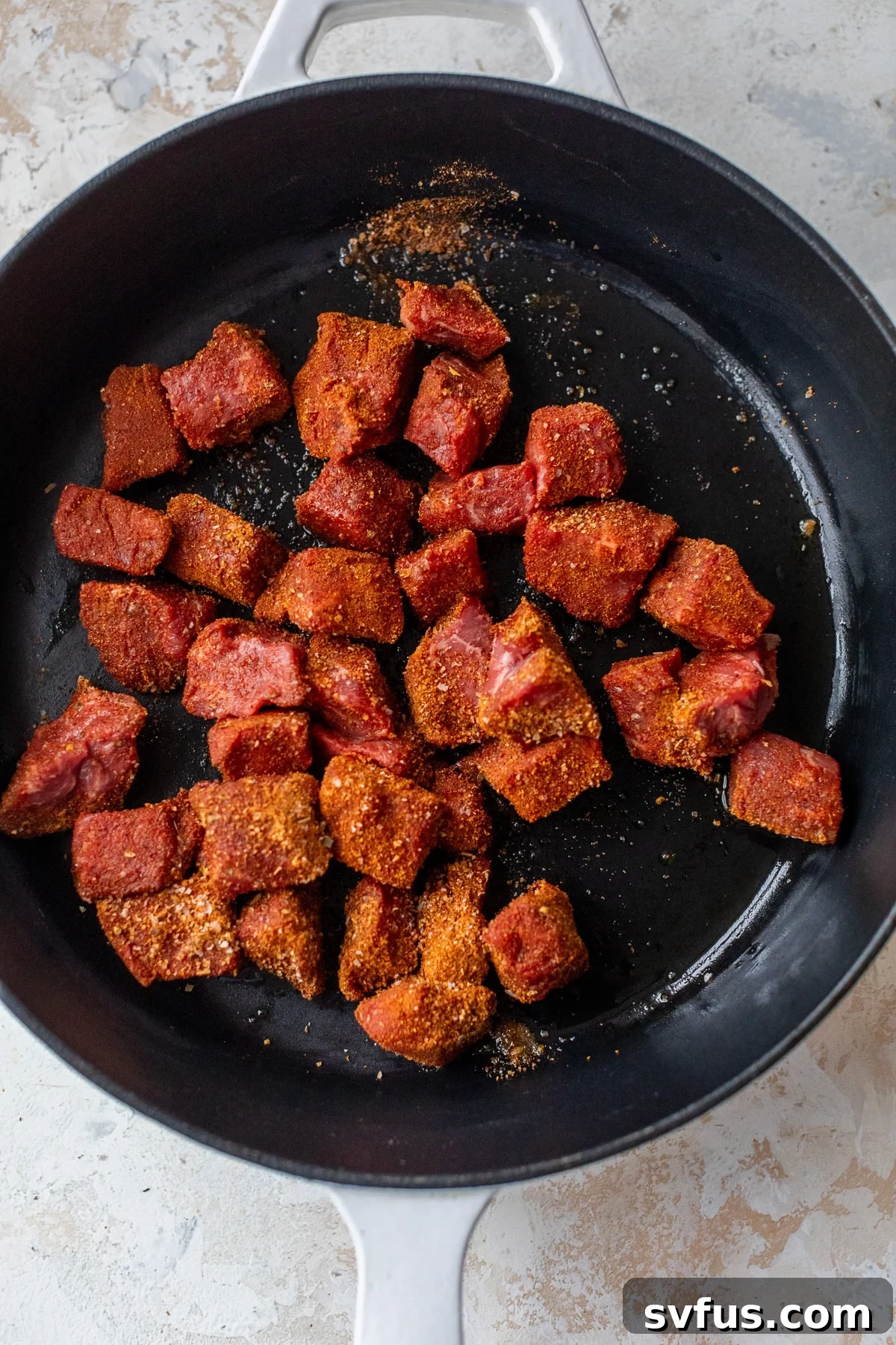 Cajun-seasoned steak pieces sizzling in a hot cast iron skillet, actively browning on all sides.