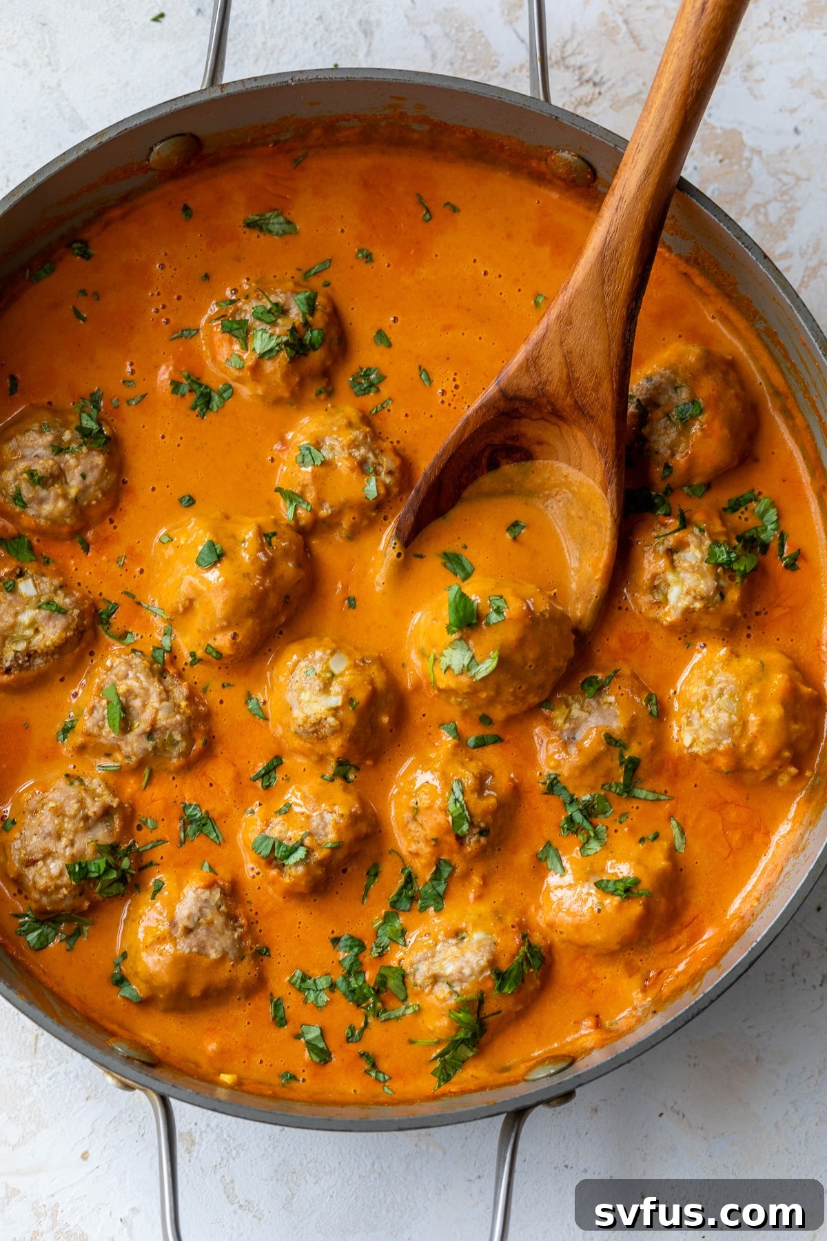 coconut curry meatballs in a skillet with a wooden spoon
