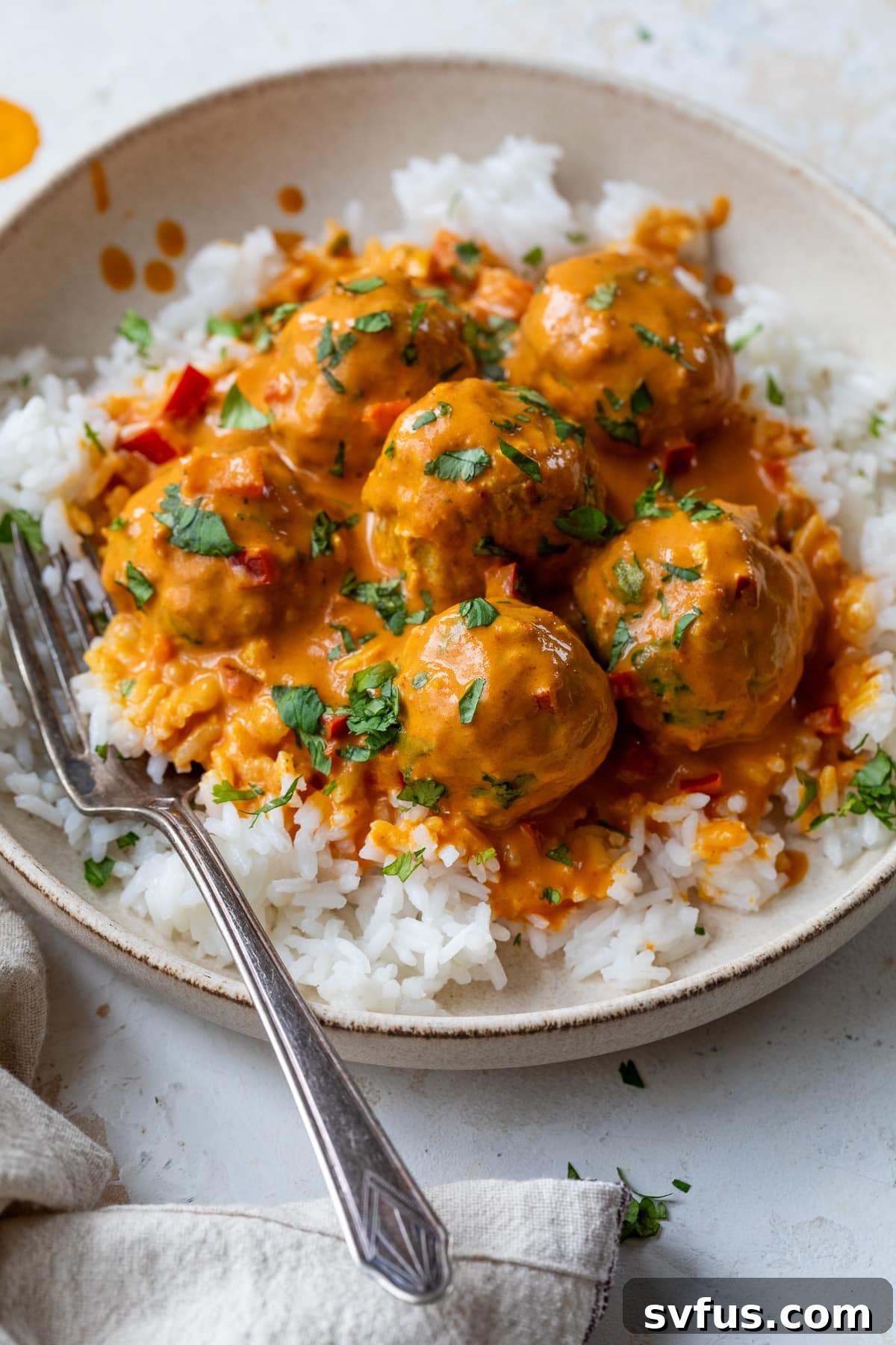 coconut curry meatballs over rice on a plate with a fork
