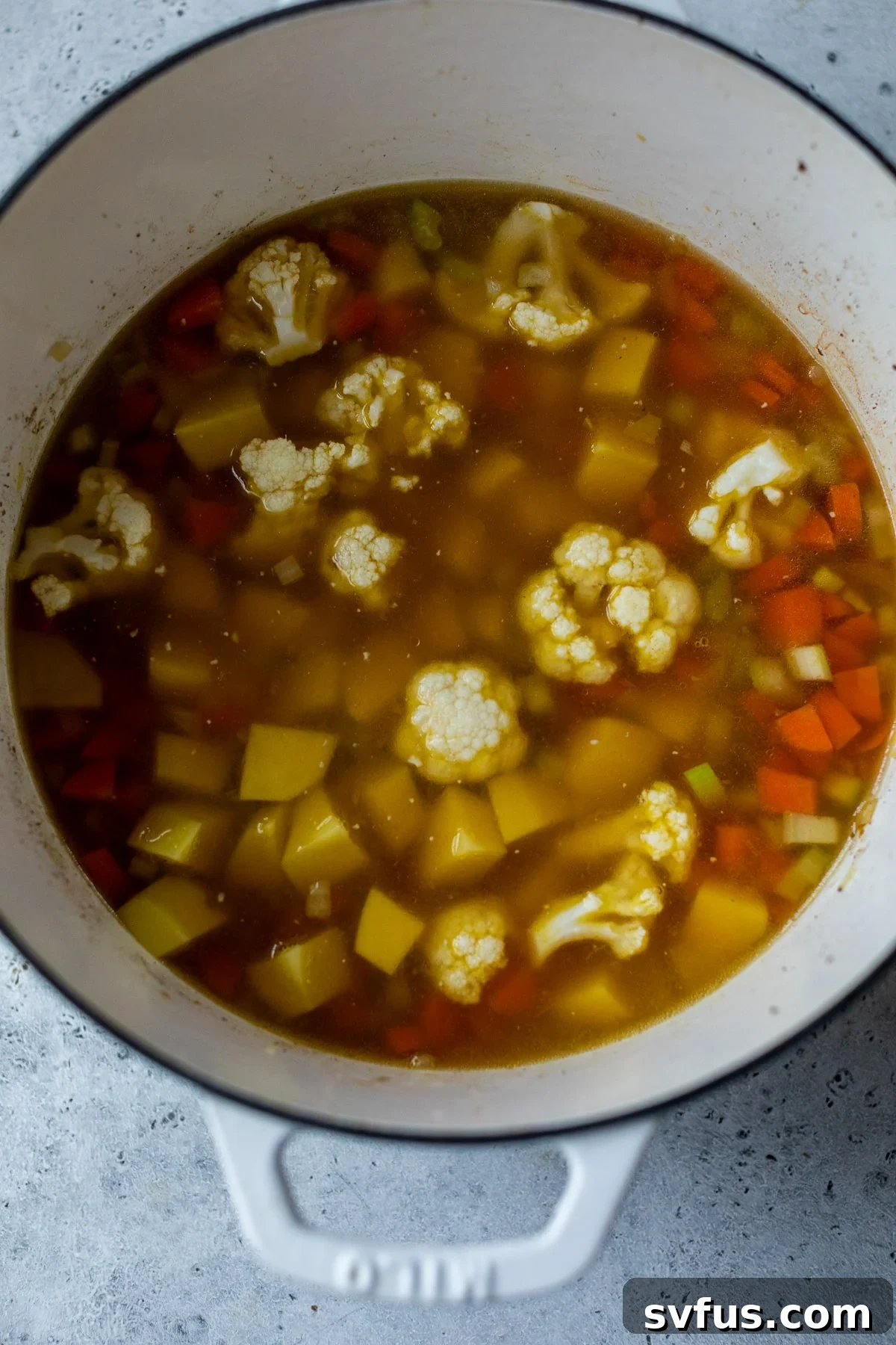 cauliflower, potatoes, and vegetables in a dutch oven with broth