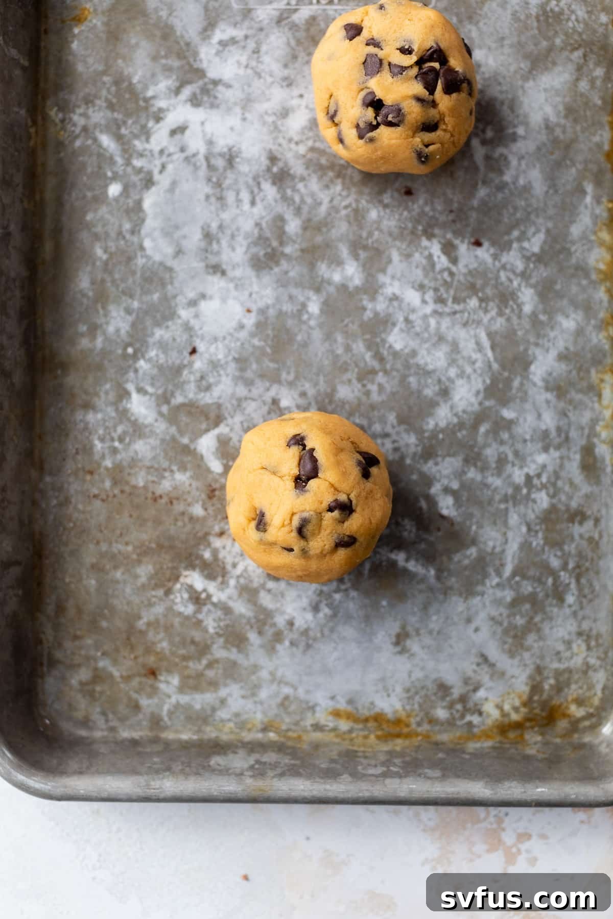 Two perfectly shaped cookie dough balls ready for baking, placed on a parchment-lined baking sheet.