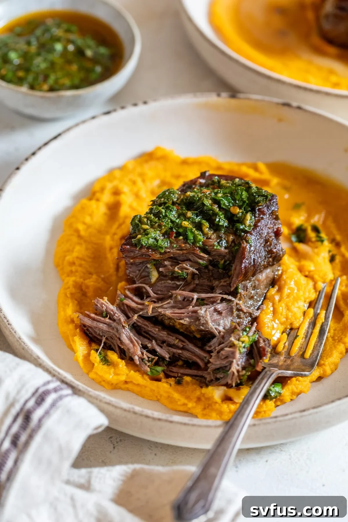 Braised boneless short ribs served with vibrant chimichurri sauce over creamy carrot puree in a modern bowl with a fork, ready to be enjoyed.
