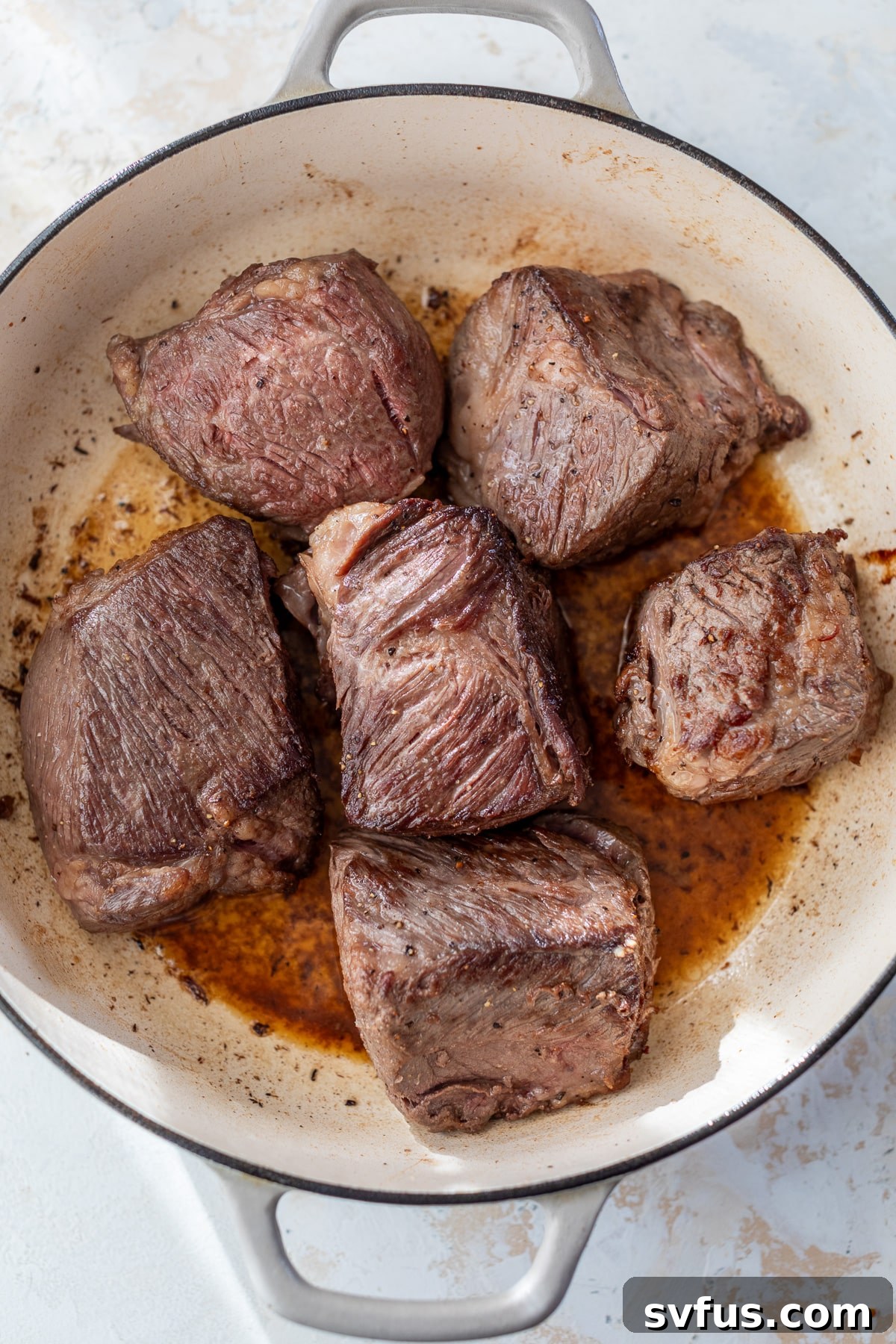 Raw boneless short ribs being seared to a golden brown in a hot Dutch oven, capturing the initial stage of flavor development.