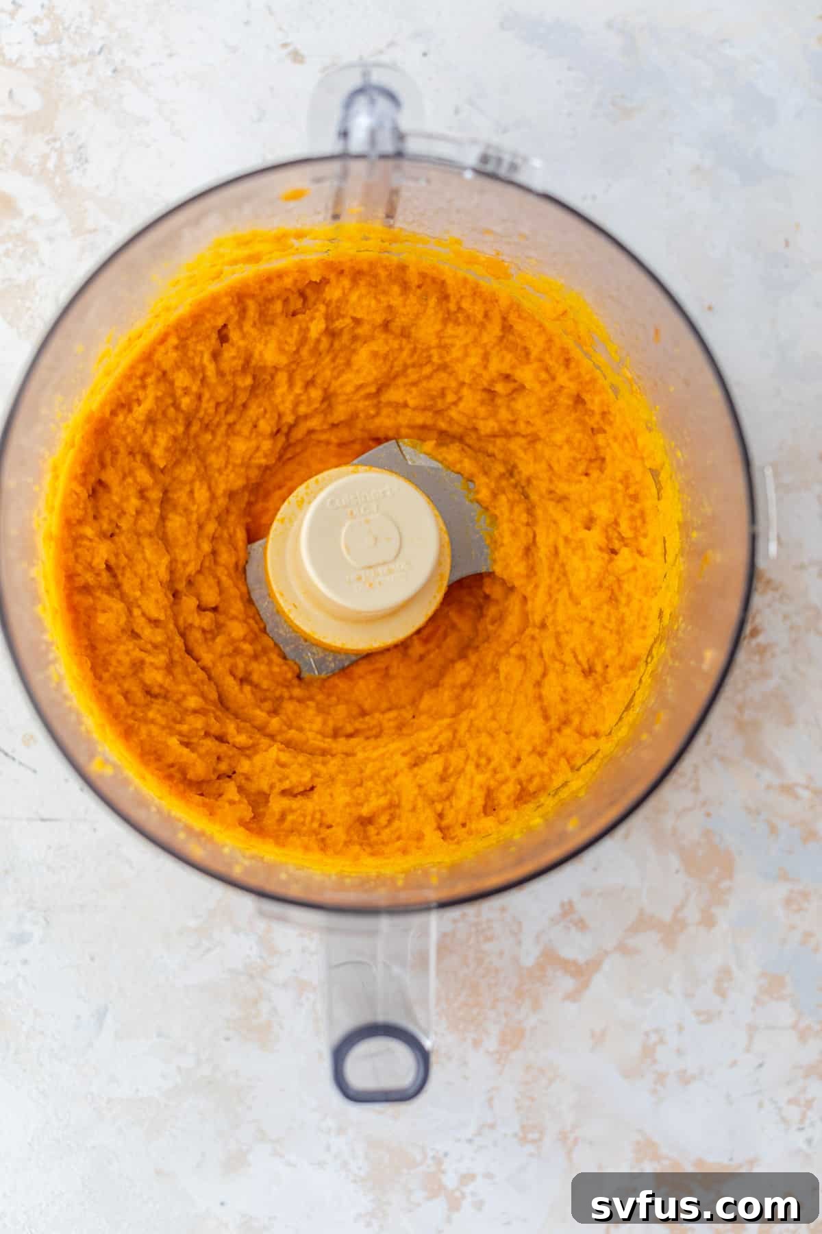 Smooth, vibrant orange carrot puree being processed in a food processor, capturing the final stages of its preparation.