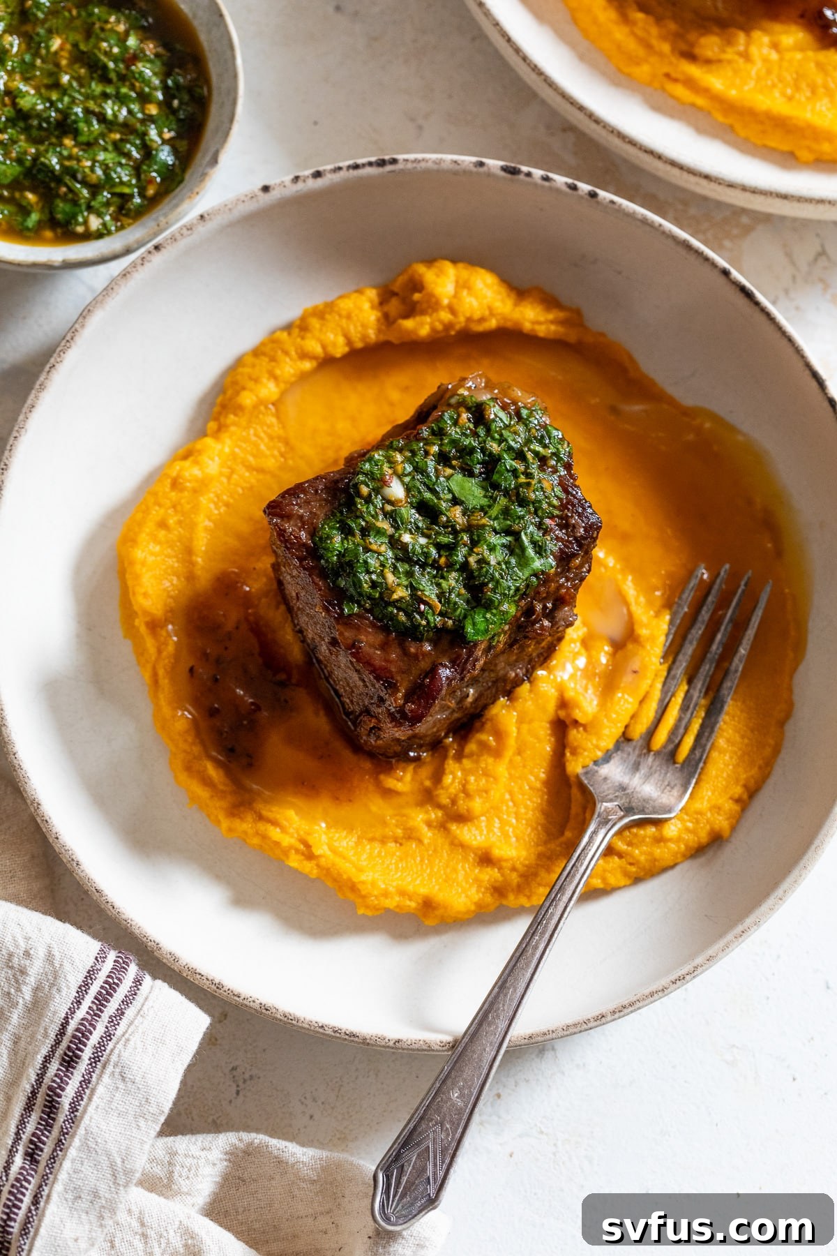 A perfectly plated dish of braised boneless short ribs with a generous dollop of creamy carrot puree, drizzled with fresh chimichurri sauce, and accompanied by a fork.