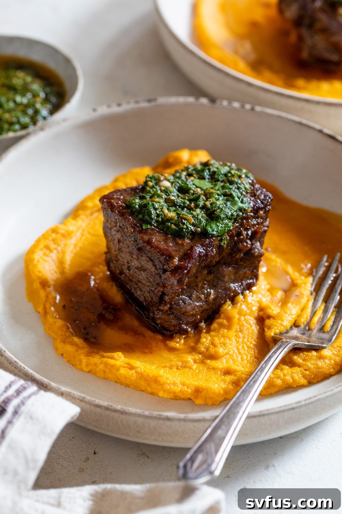 Close-up of a bowl of braised boneless short ribs, perfectly tender, served with bright green chimichurri and creamy carrot puree, highlighting the textures and colors of the dish.