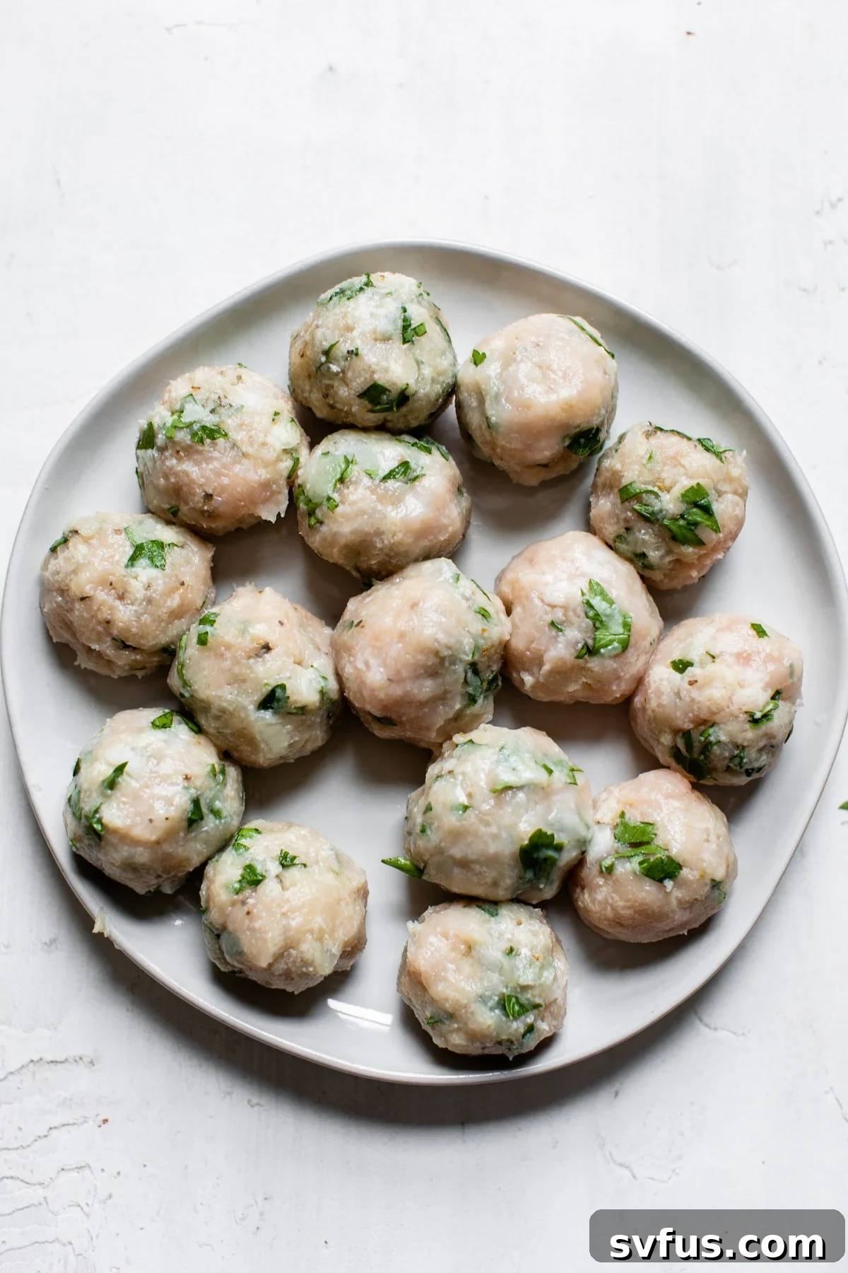 Uncooked, perfectly formed chicken meatballs neatly arranged on a plate, ready for the skillet.