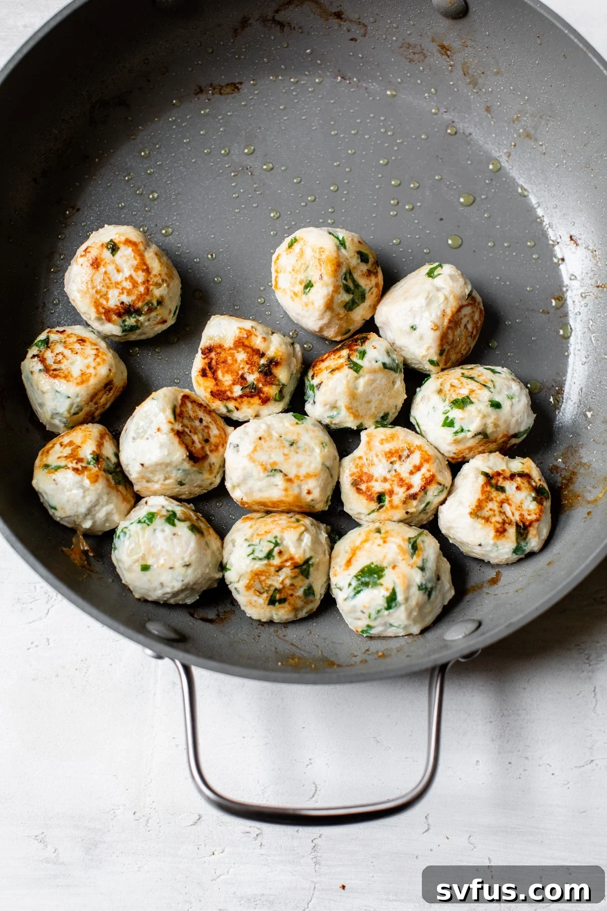 Sizzling golden-brown chicken meatballs searing to perfection in an oven-safe cast-iron skillet.
