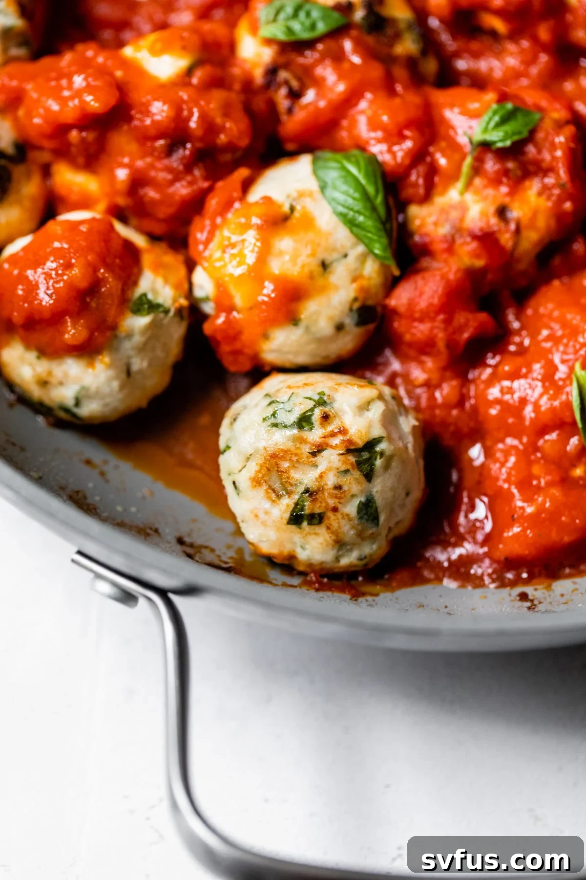 Perfectly baked chicken meatballs bathing in a rich roasted garlic marinara sauce in a skillet, garnished with fresh basil and ready to serve.