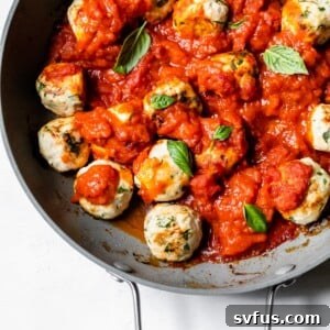 Close-up of baked chicken meatballs in a skillet with marinara sauce, garnished with fresh herbs.