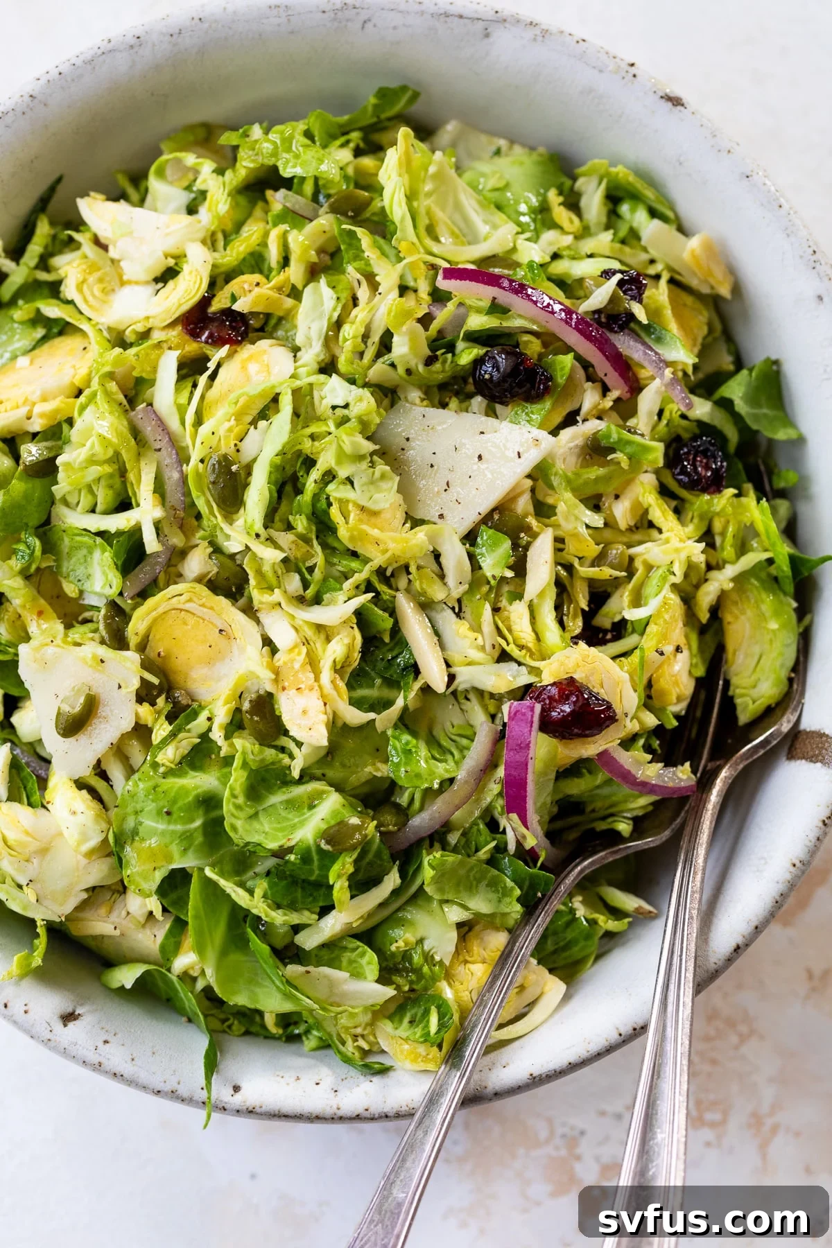 Fresh Brussels Sprouts Slaw in a decorative bowl with a serving fork and spoon, ready to be enjoyed.