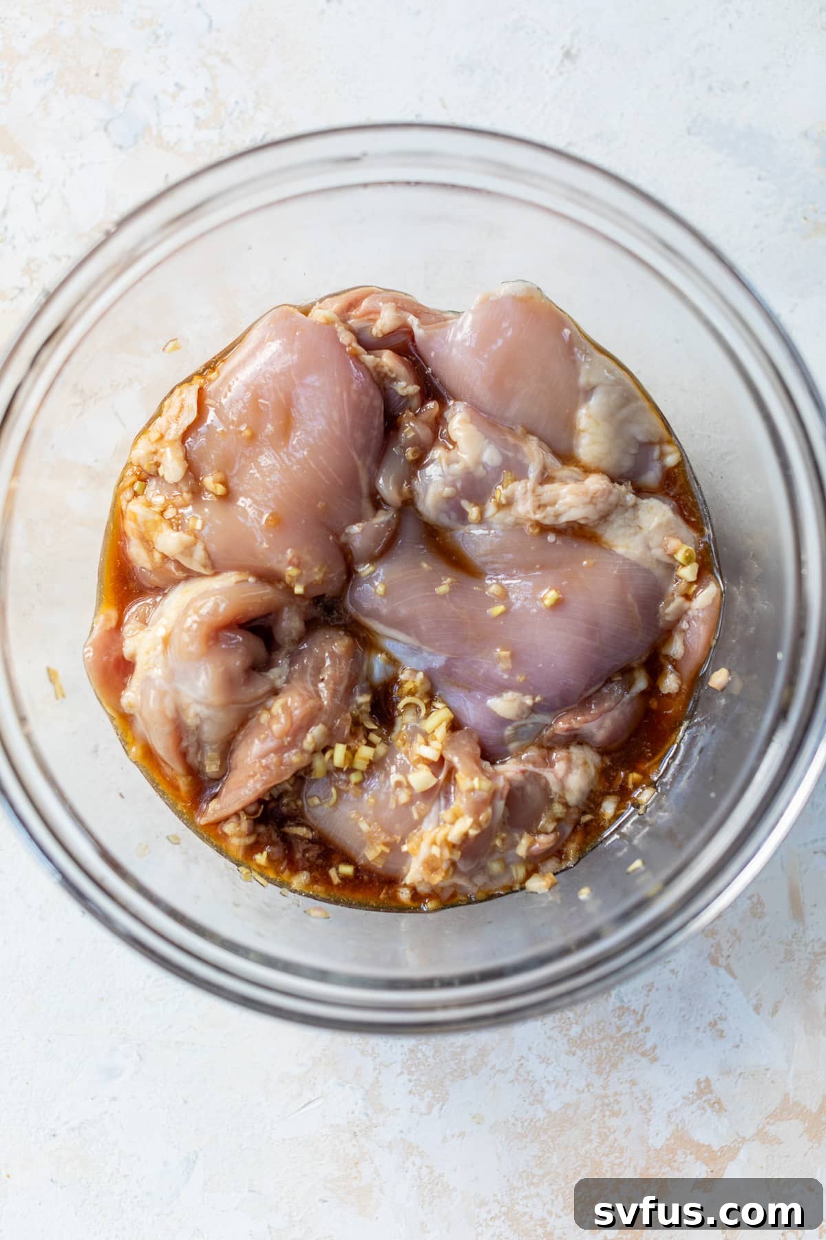 Chicken thighs being added to a bowl with marinade ingredients.
