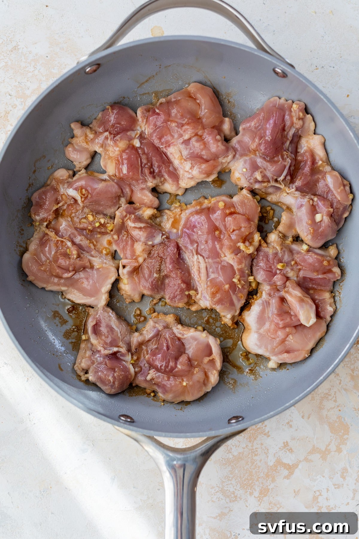 Chicken thighs being placed in a hot skillet for searing.