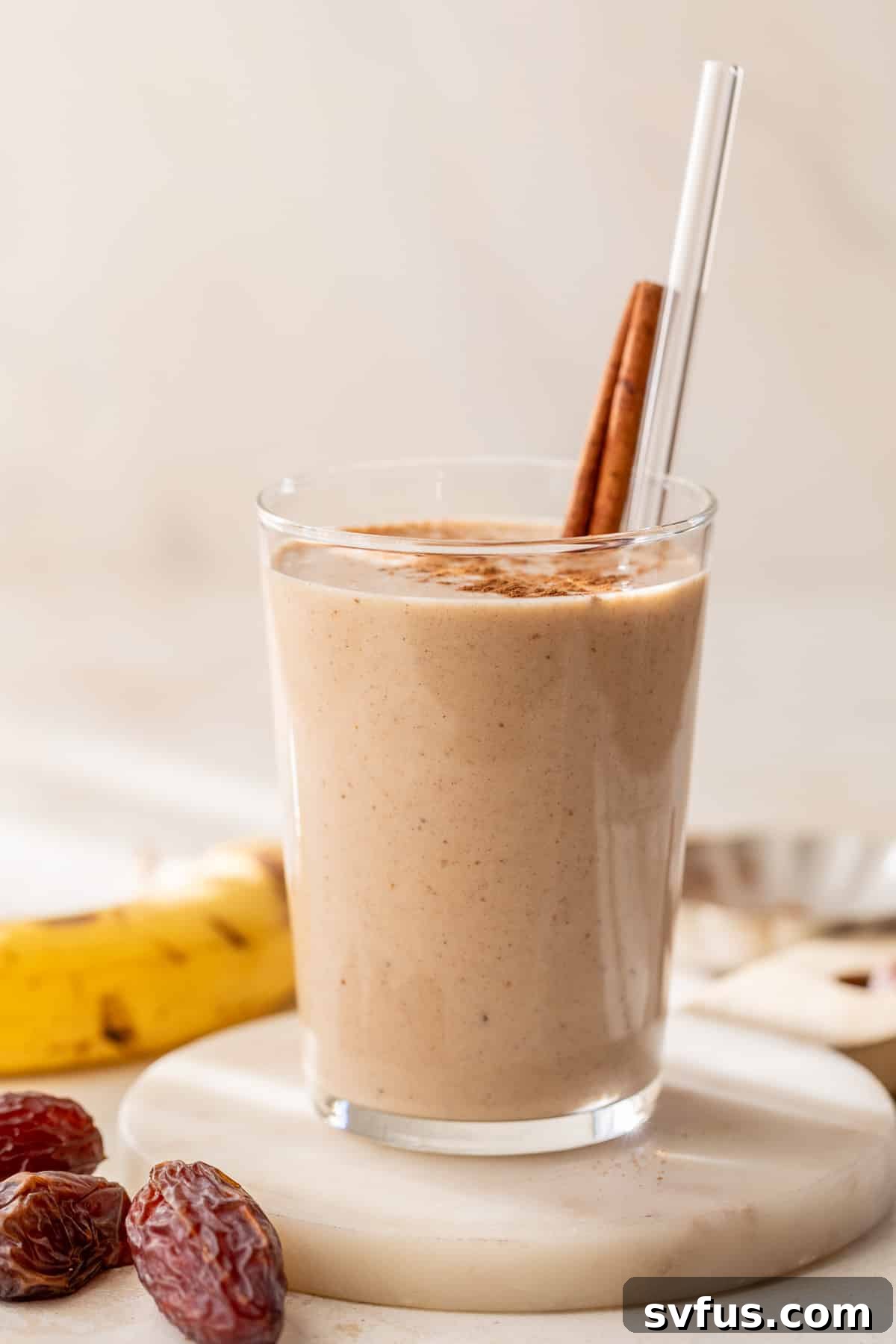 side view of a date smoothie in a glass with a straw and cinnamon stick against a bright background