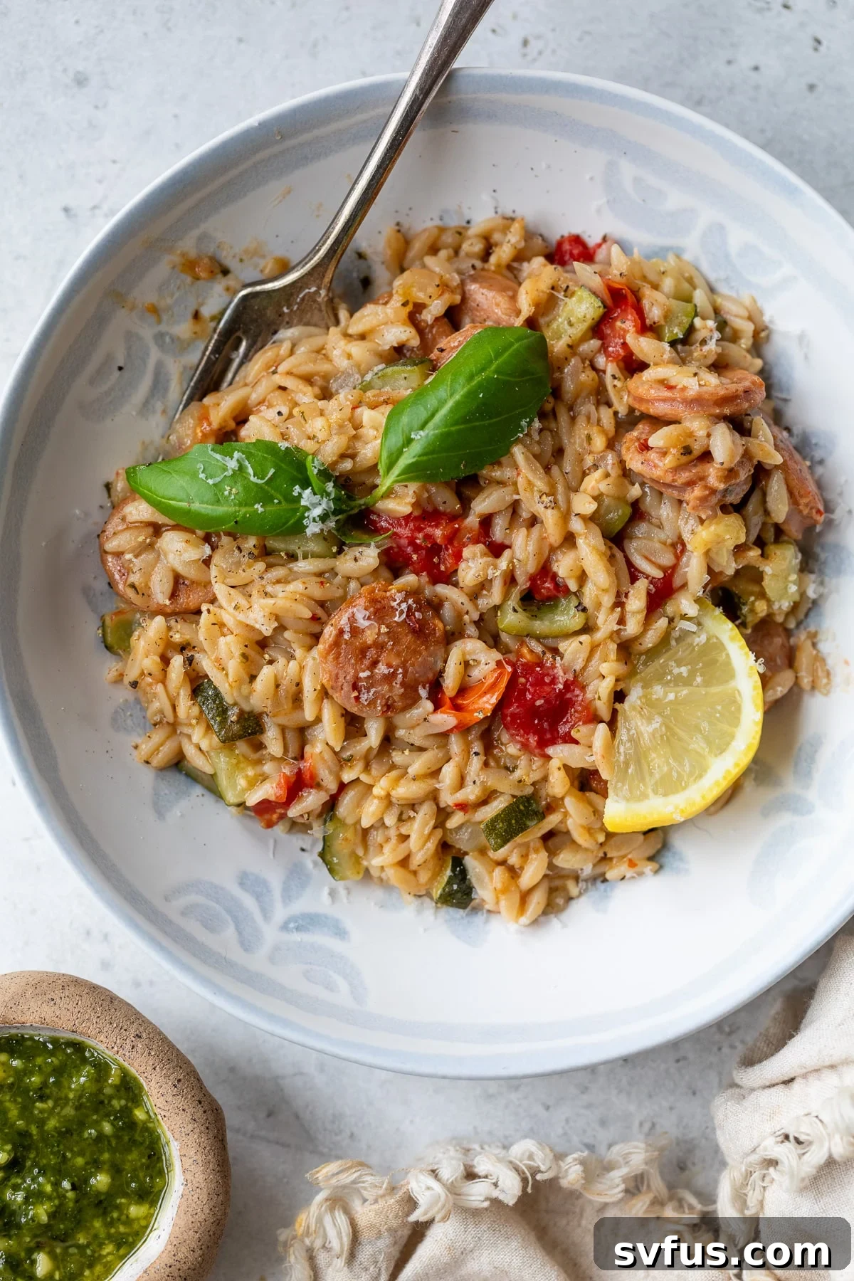 Creamy chicken sausage orzo served in a bowl with a fork, garnished with fresh herbs.