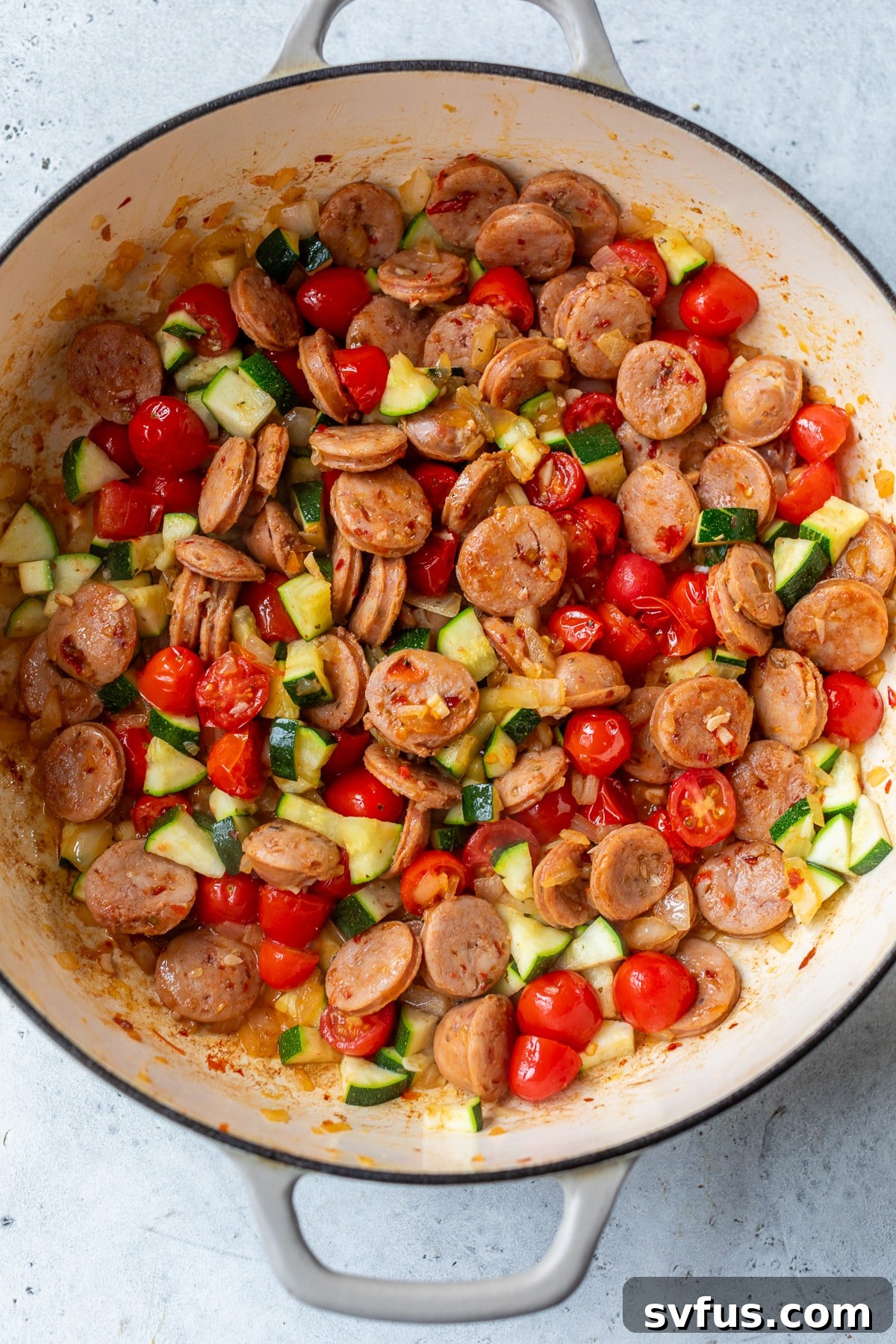 Chicken sausage and colorful vegetables simmering in a Dutch oven, releasing aromatic steam.