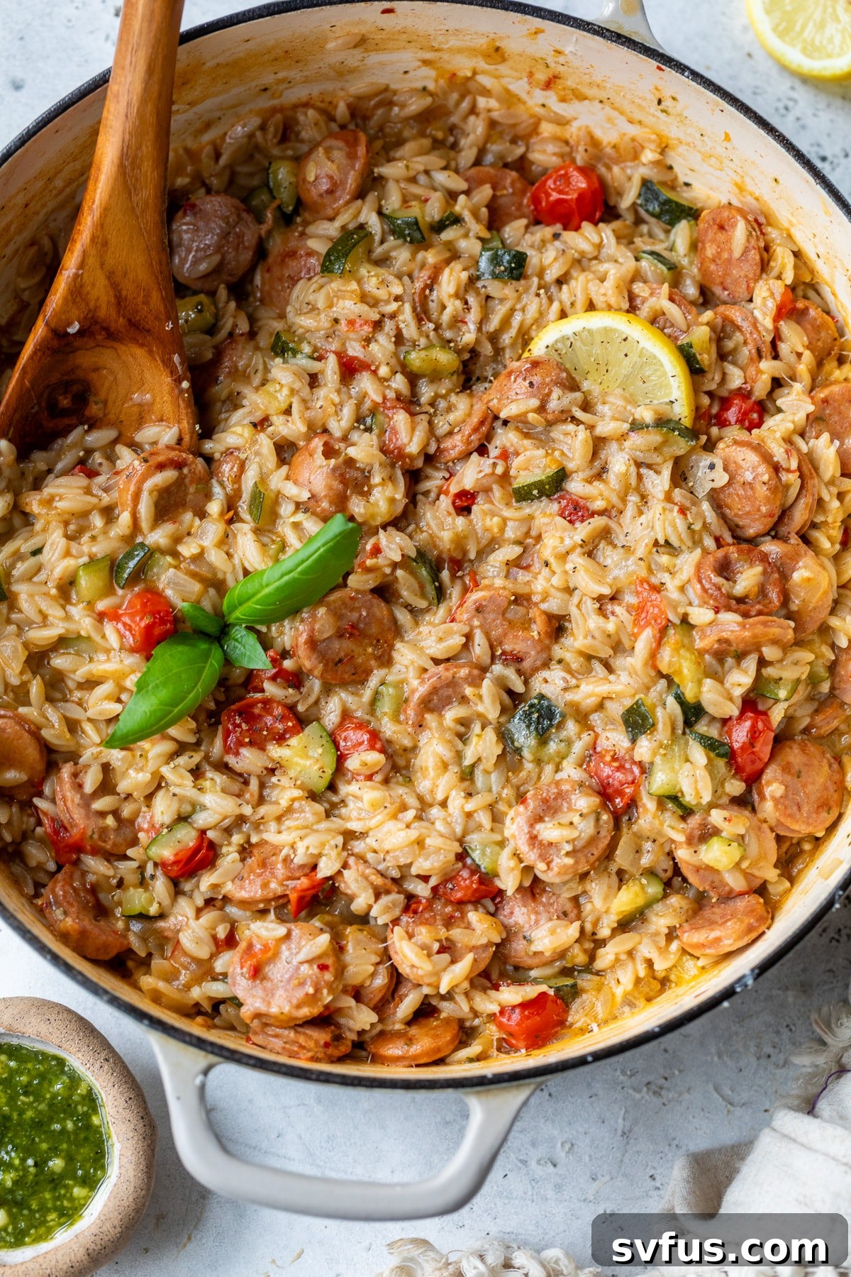 Finished creamy chicken sausage orzo in a Dutch oven with a wooden spoon, garnished with fresh basil.
