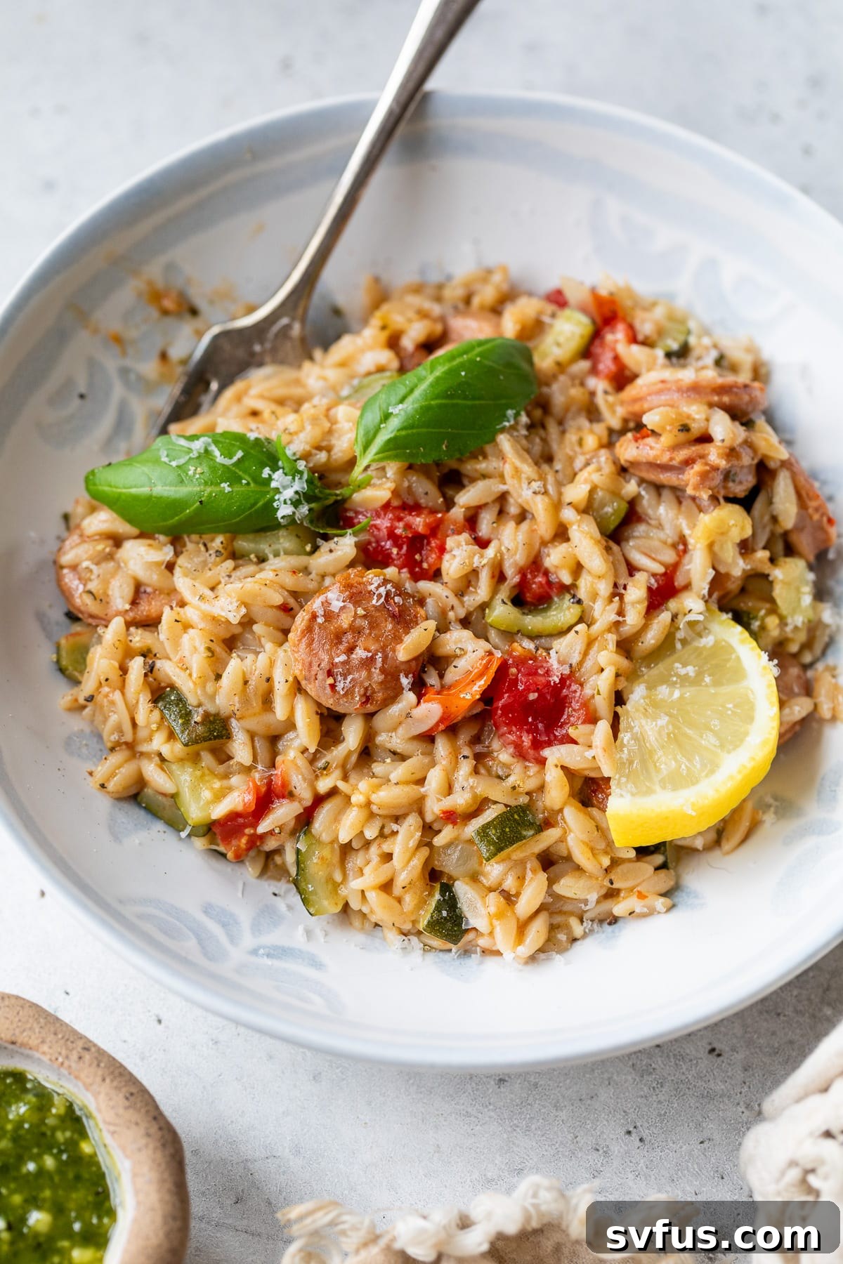 A serving of creamy chicken sausage orzo in a white bowl, ready to be eaten, with a fork resting in it.