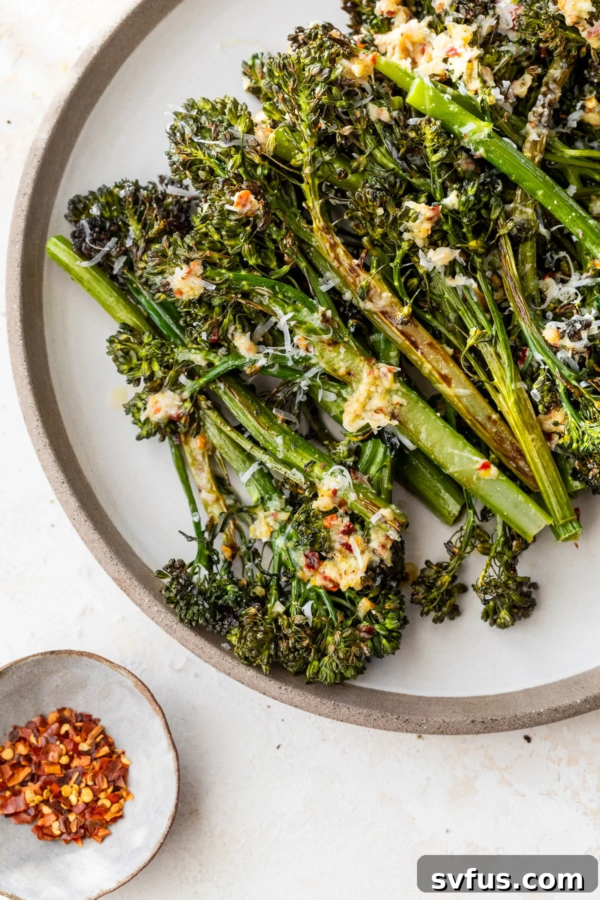 A vibrant plate of roasted broccolini, garnished with lemon wedges and grated parmesan cheese, ready to be served.