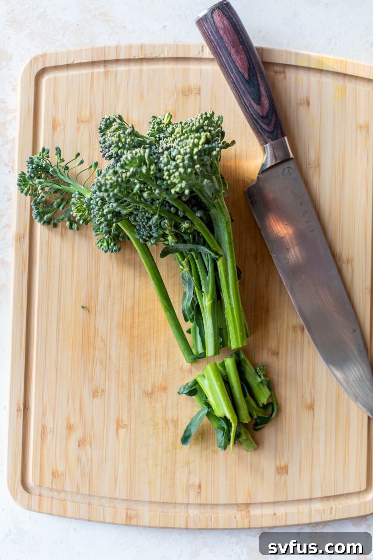 Fresh broccolini and a knife on a cutting board, illustrating the trimming and slicing process.