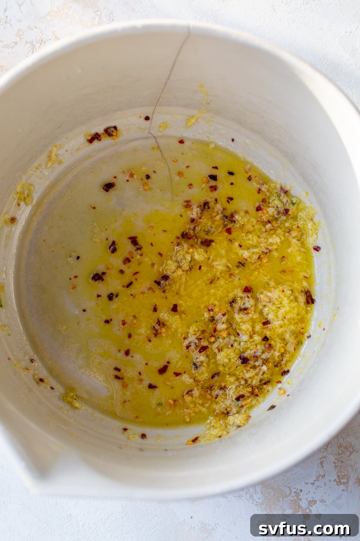 A bowl containing lemon juice, red pepper flakes, grated parmesan cheese, olive oil, and salt, ready to be whisked into a sauce.