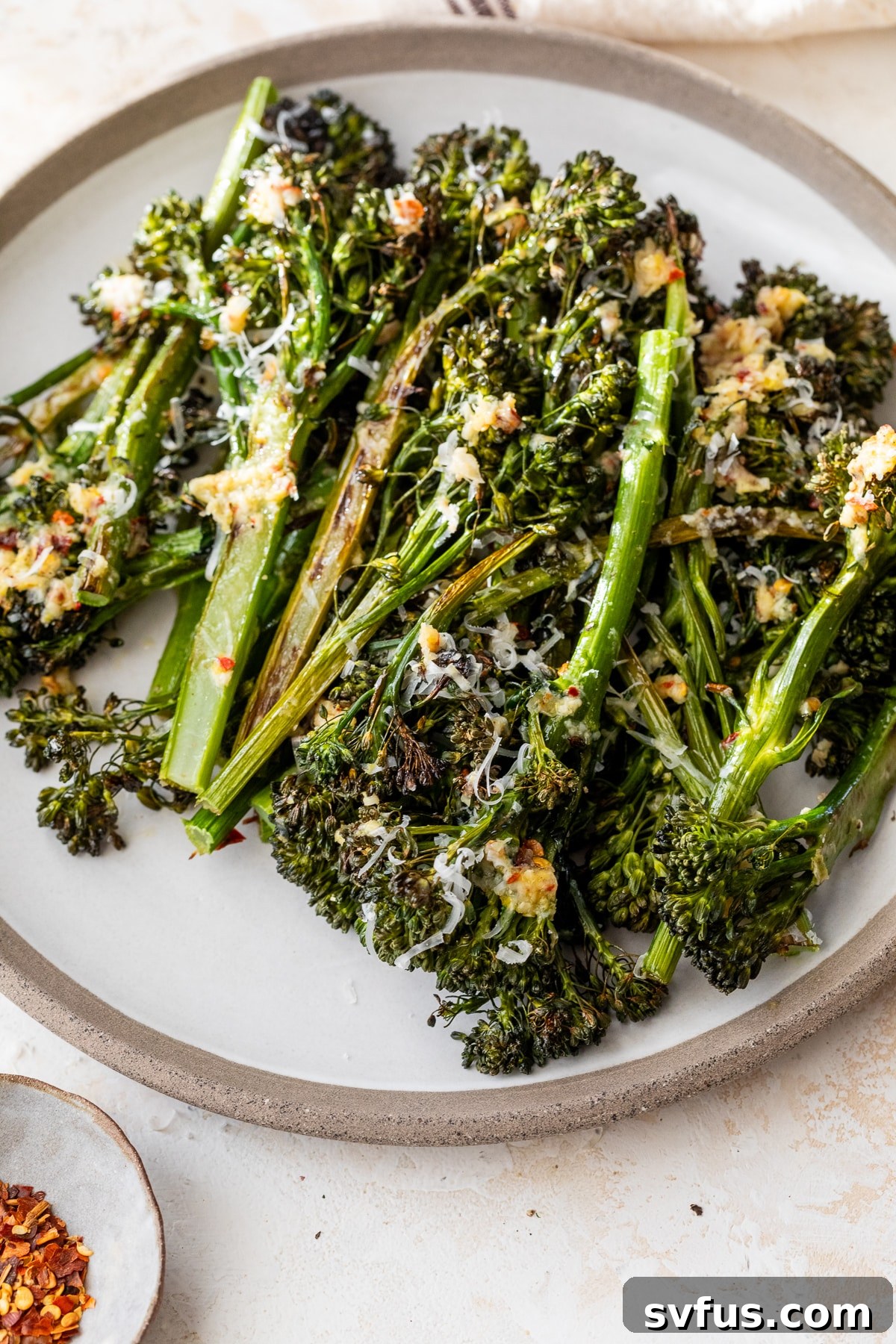 A close-up shot of roasted broccolini on a white plate, showcasing its vibrant green color and tender texture, garnished with fresh lemon.