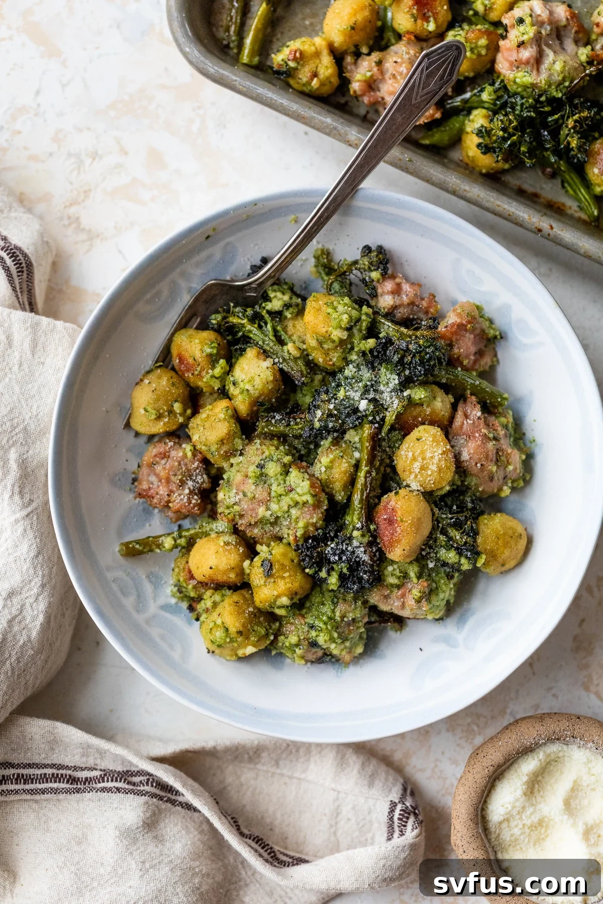 A delicious bowl of Sheet Pan Gnocchi with sausage and broccolini, garnished with fresh basil and parmesan.