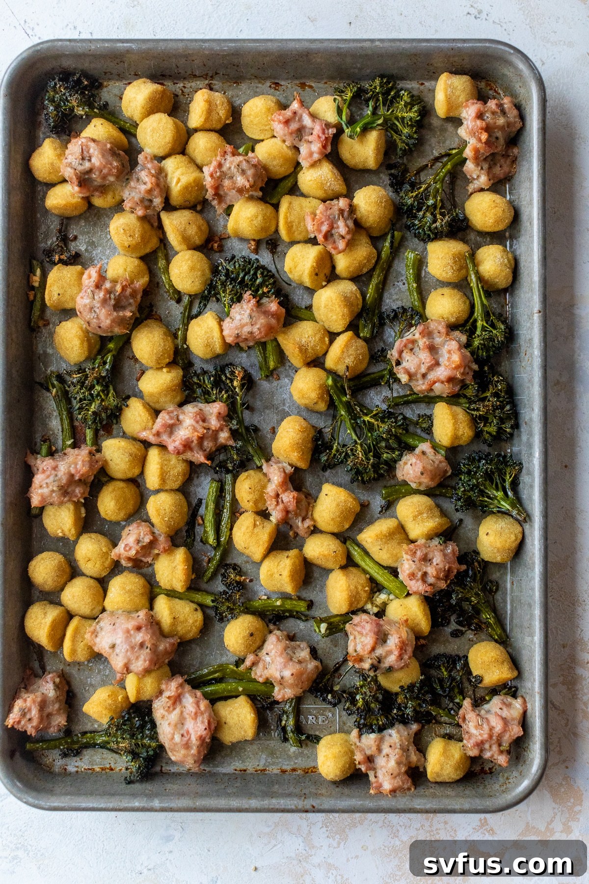 Gnocchi, broccolini, and Italian sausage arranged on a baking sheet, ready for the oven.