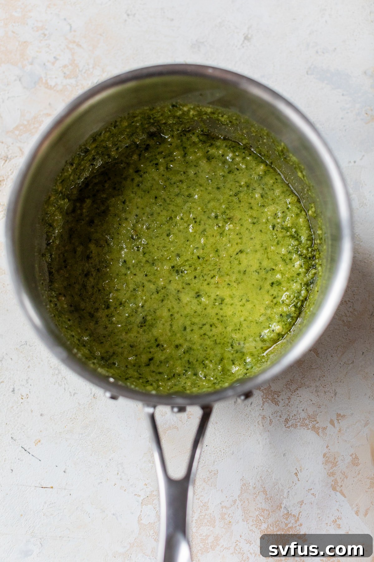 Creamy pesto sauce gently heating in a small saucepan on the stovetop.