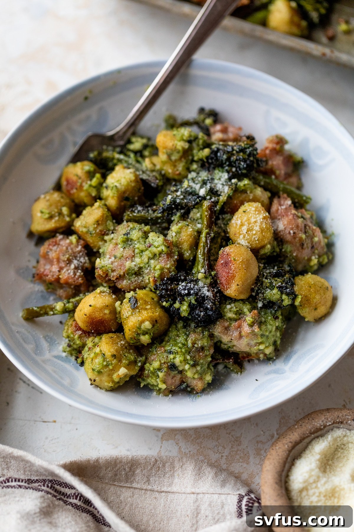 Close-up of a fork scooping a bite of Sheet Pan Gnocchi with sausage and broccolini from a bowl.