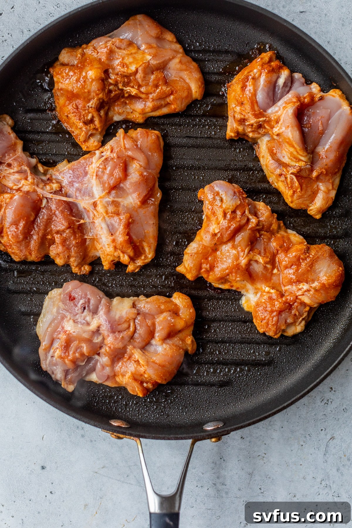 Raw chipotle chicken thighs sizzling in a hot black grill pan, showing early charring.