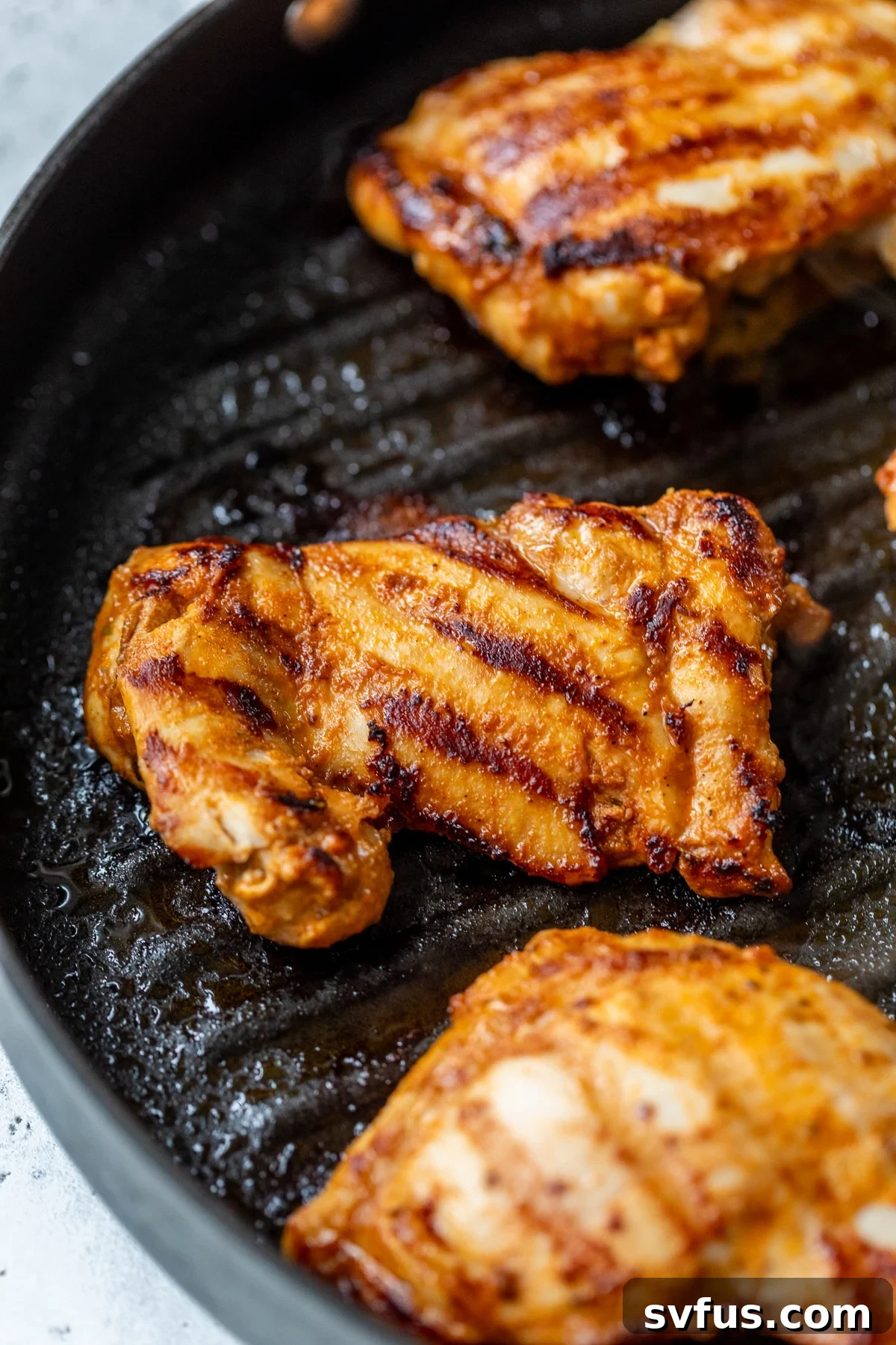 Grilling chipotle chicken thighs in a black skillet, showing steam and browning.