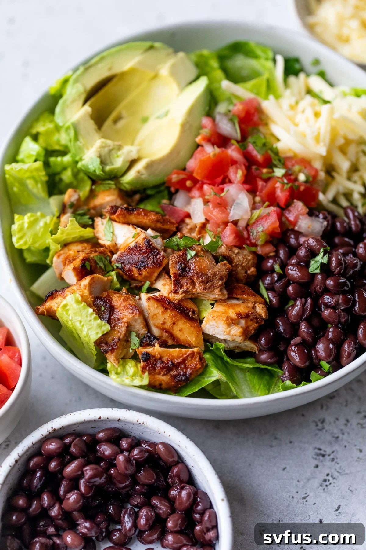 A vibrant and colorful burrito bowl generously topped with sliced grilled chipotle chicken, black beans, salsa, shredded cheese, and creamy avocado.