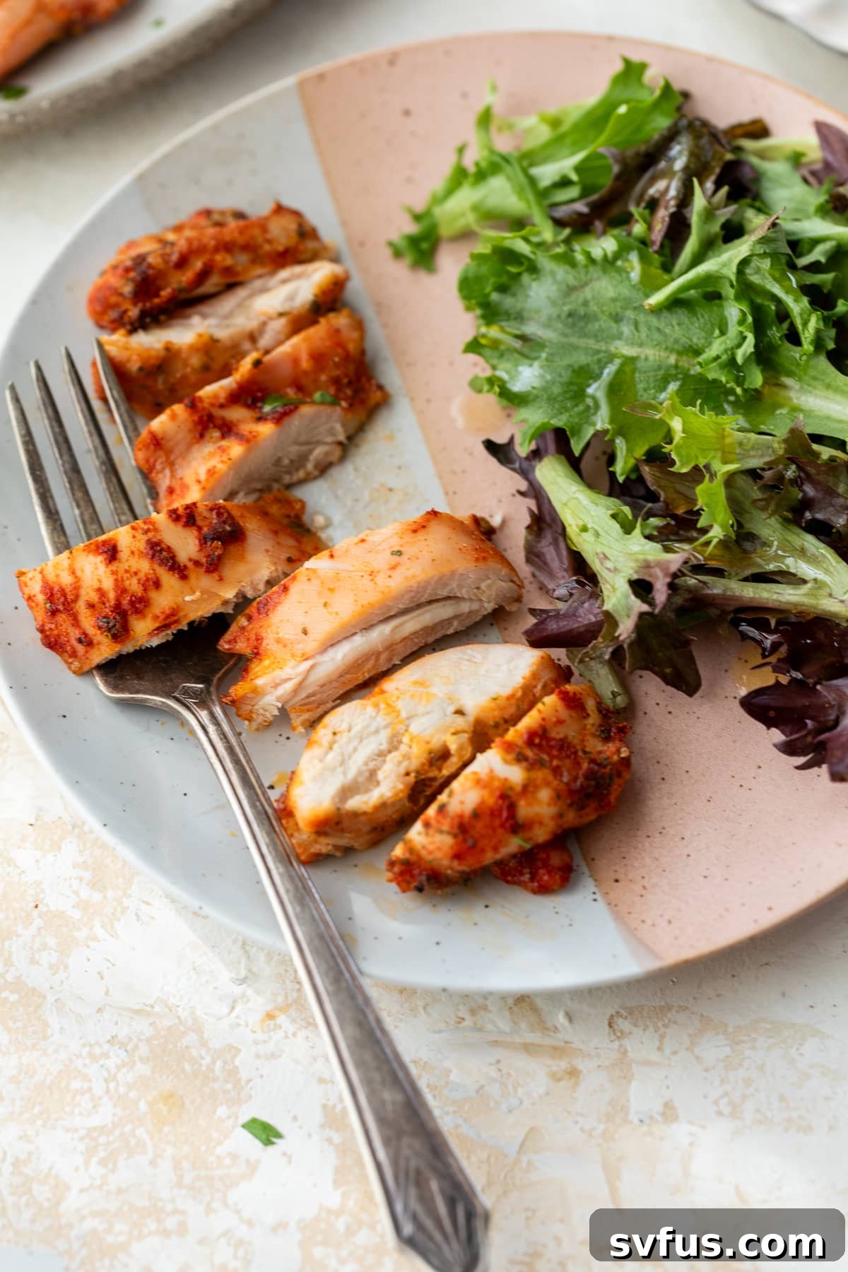 baked boneless chicken thighs sliced on a plate with mixed greens and a fork