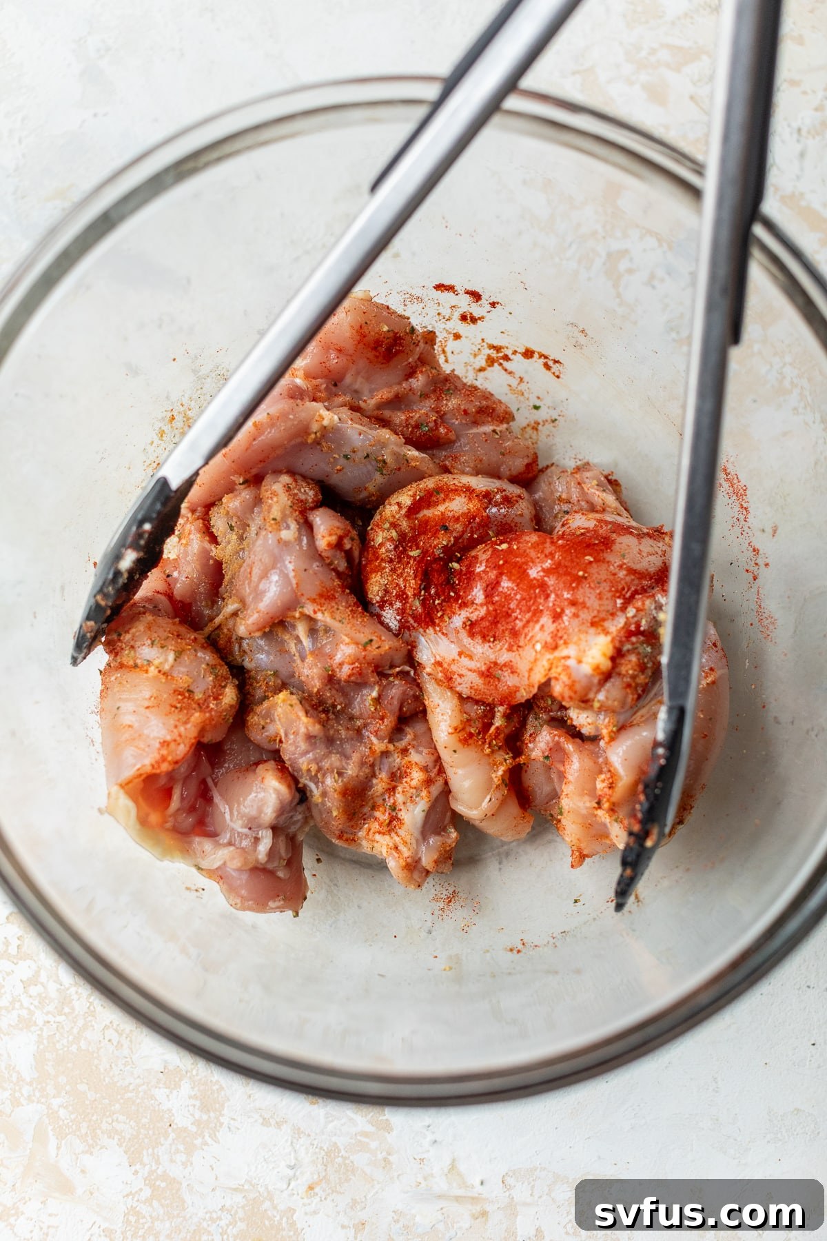 chicken thighs added to a glass bowl and tossed together with spices