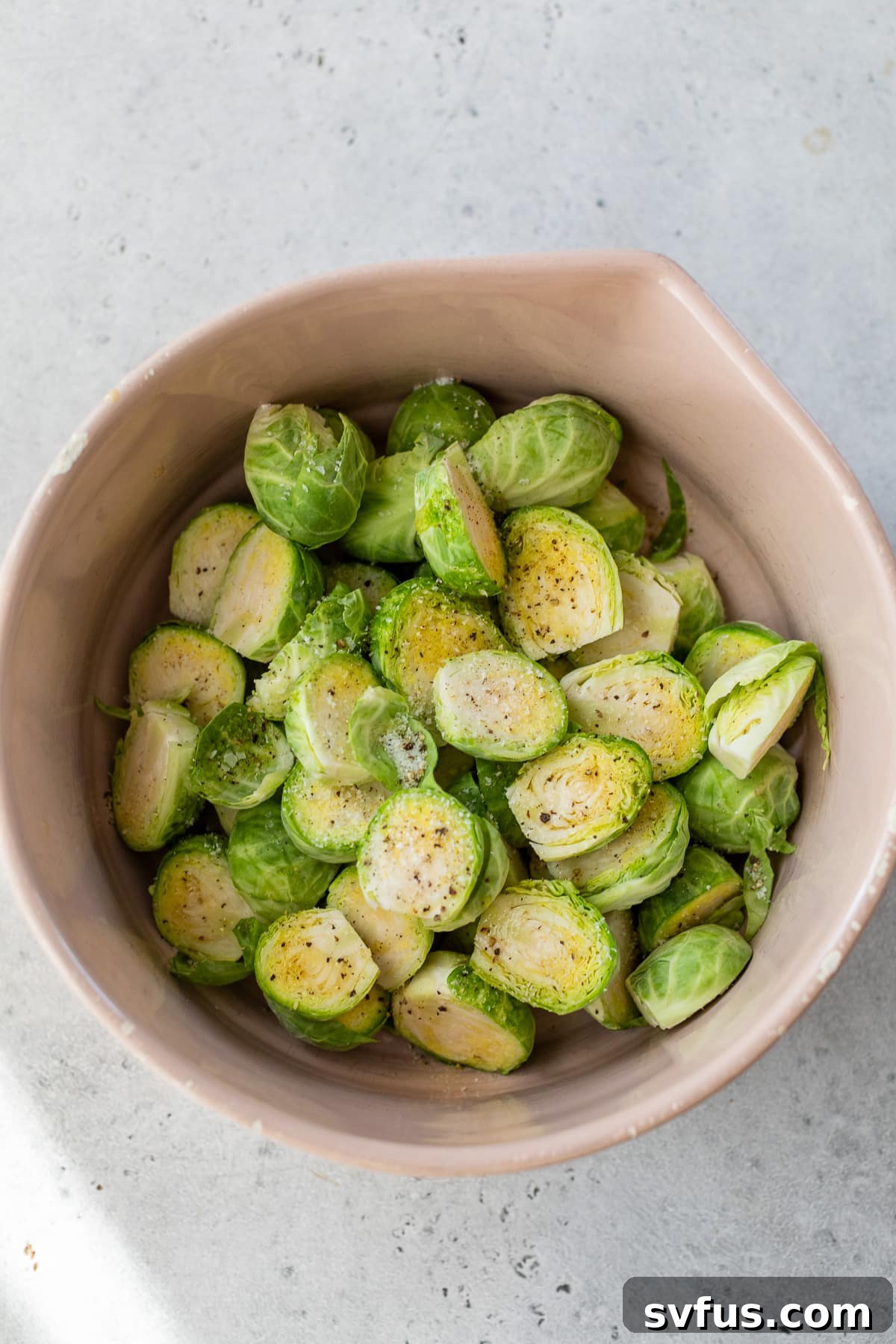 Sliced Brussels sprouts in a bowl, seasoned with salt and black pepper, ready for the air fryer