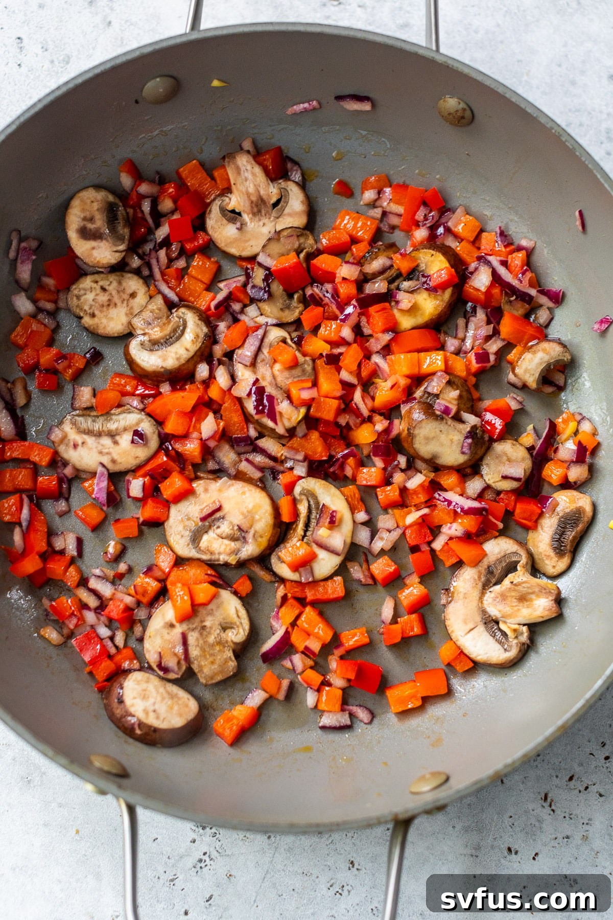 Diced red peppers, onions, and sliced mushrooms cooking in a large skillet, becoming tender and aromatic.