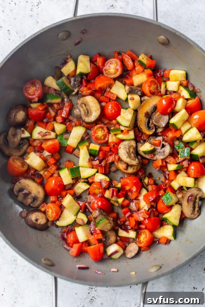 A mix of colorful vegetables, including zucchini and tomatoes, cooking in a large skillet, looking tender and vibrant.